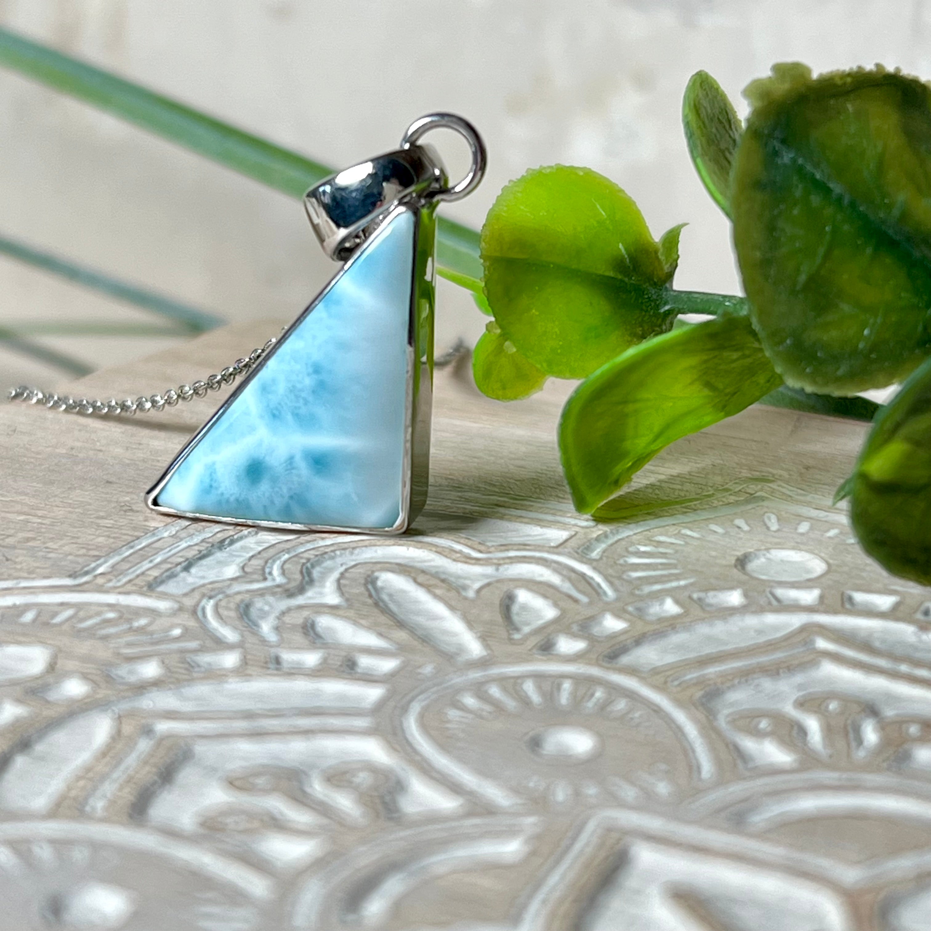Larimar Anhänger in markanter Dreiecksform, eingefasst in rhodiniertes 925 Sterling Silber, vor strukturiertem Hintergrund mit grünen Blättern – stilvoller Edelsteinschmuck mit karibischem Flair.