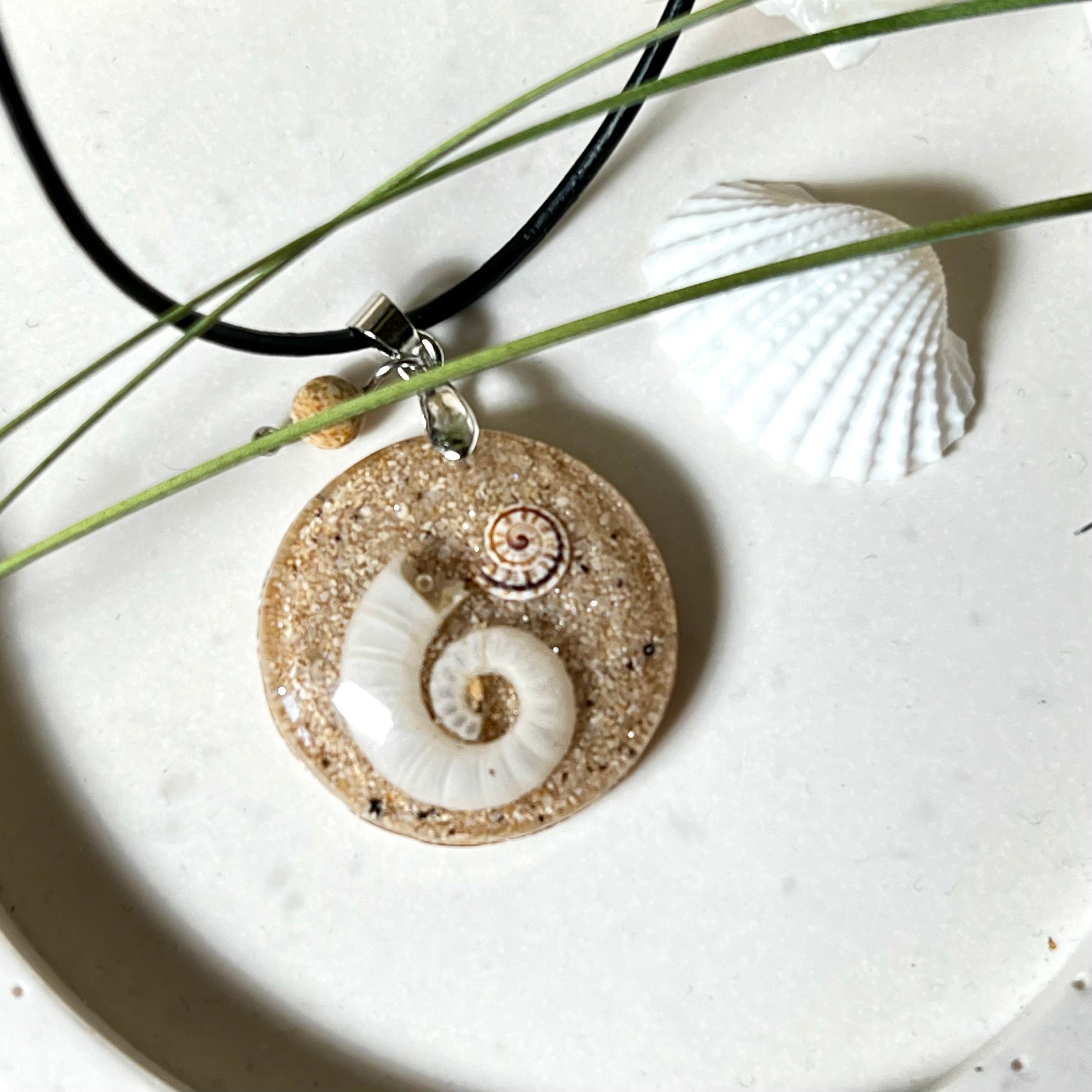 Handgemachter Anhänger mit echter Spirale, kleiner Schnecke, Meersand und feinem Glitzereffekt im Harz. Verziert mit einer Jaspisperle, Edelstahlöse und Lederkette mit Verlängerung. Maritimer Natur-Schmuck, inspiriert vom Ozean