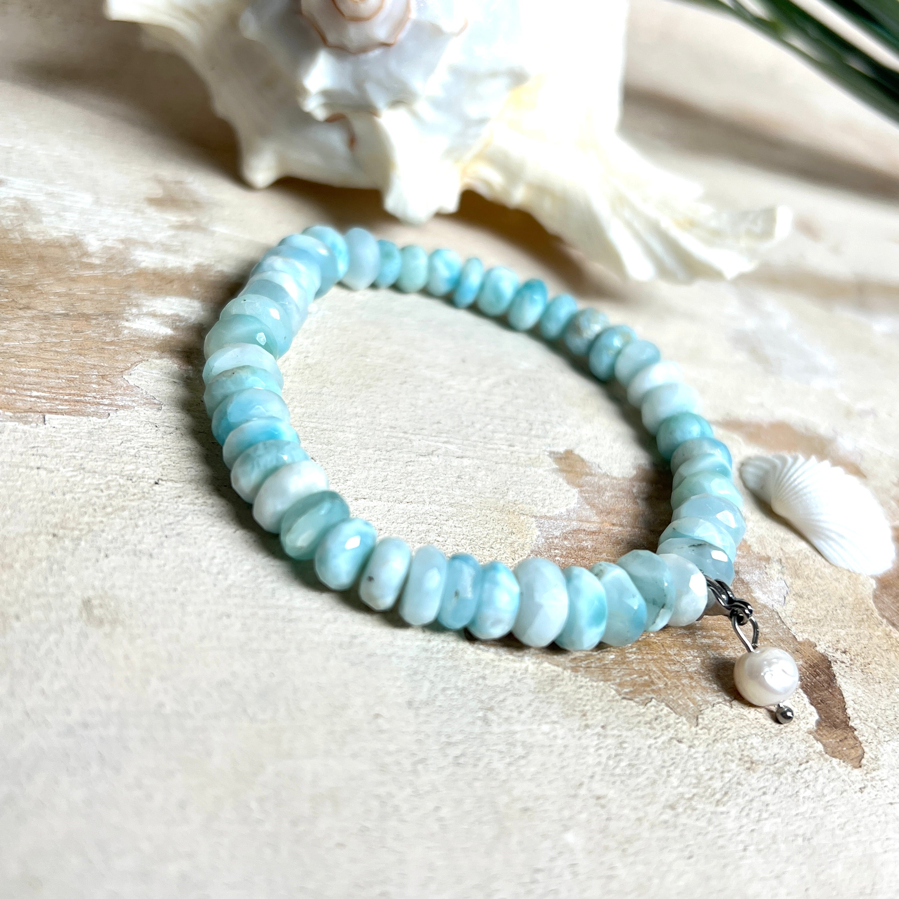 Handgefertigtes Armband aus seltenem Larimar mit facettierten, türkis-blauen Edelsteinperlen (Ø ca. 6–7 mm), elastischem Band und einem zarten Süßwasserperlen-Charm an Edelstahlkarabiner. Der wertvolle Larimar, auch „Stein des Atlantis“ genannt, gilt als Edelstein der Ruhe und Meeresverbundenheit.