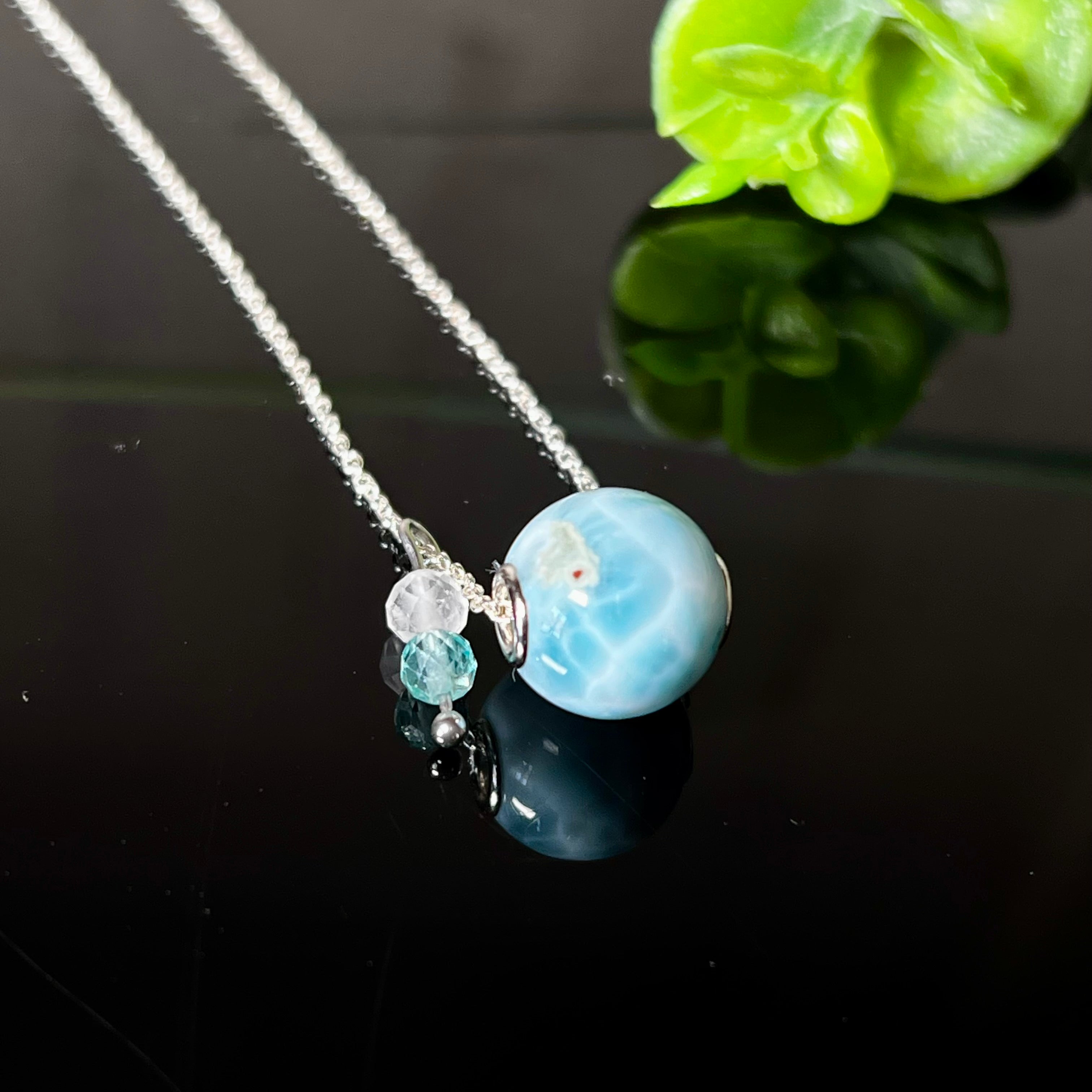 Feine Halskette aus 925er Silber mit einer polierten Larimar-Perle als Hauptstein, ergänzt durch funkelnde Apatit- und Bergkristall-Perlen. Der Edelstein mit seiner typischen Meeresfärbung erinnert an tropische Lagunen und steht für innere Ruhe und Klarheit.Ideal als Geschenk zum Geburtstag, für Meerliebhaber oder spirituelle Schmuckträgerinnen.