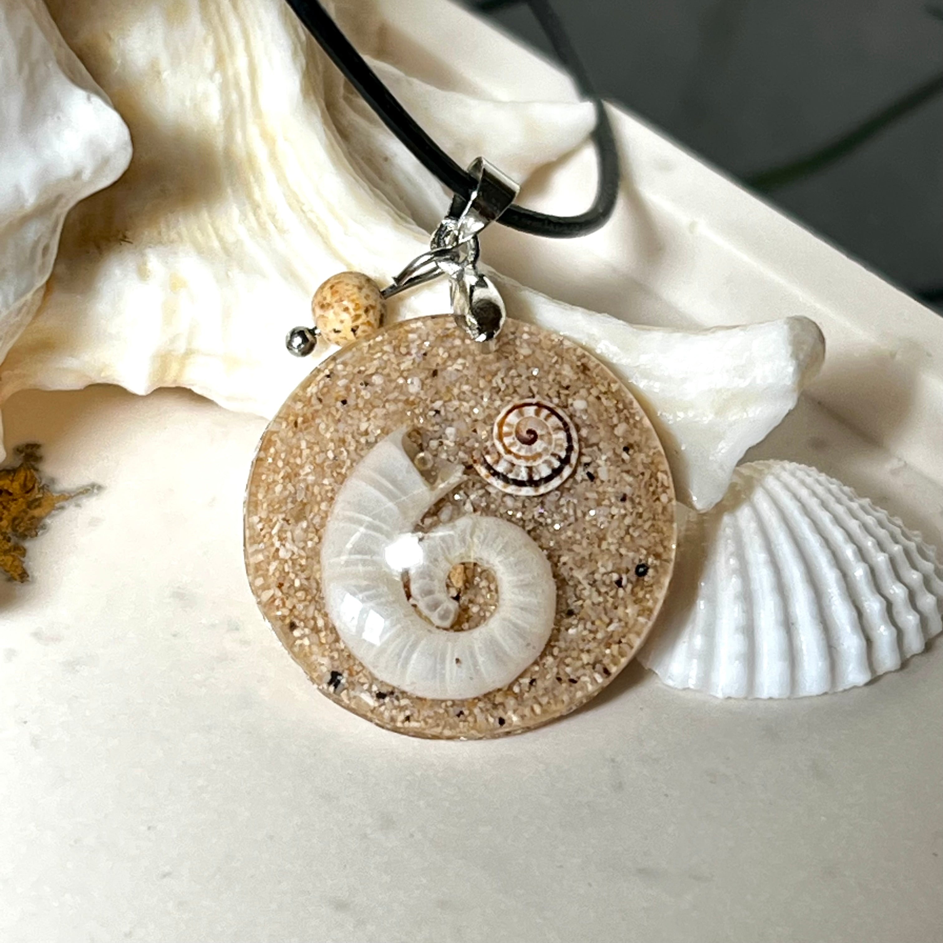 Handgemachter Anhänger mit echter Spirale, kleiner Schnecke, Meersand und feinem Glitzereffekt im Harz. Verziert mit einer Jaspisperle, Edelstahlöse und Lederkette mit Verlängerung. Maritimer Natur-Schmuck, inspiriert vom Ozean