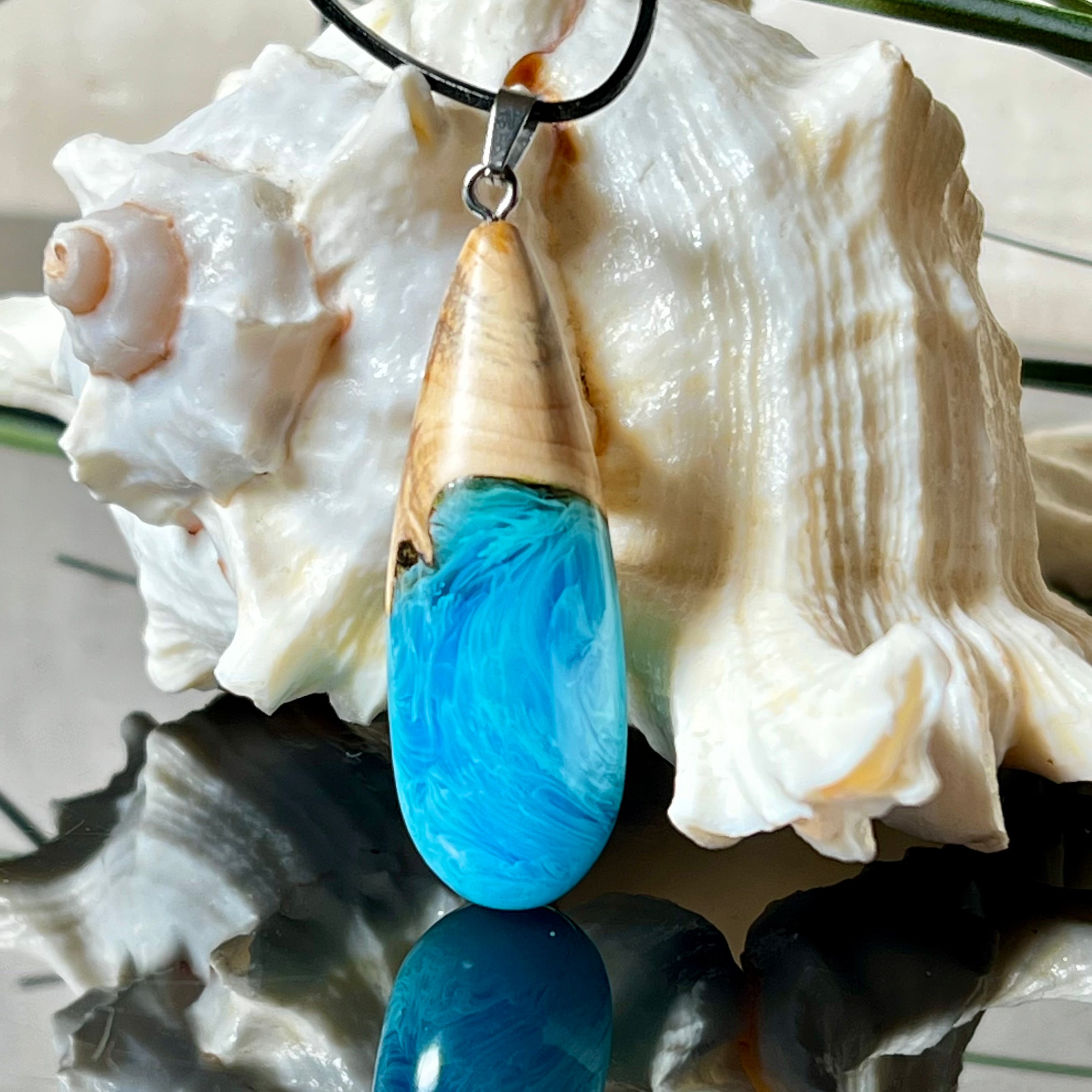 Tropfenförmiger Anhänger aus Maserholz und Harz in leuchtenden Blautönen und Weiß. Inspiriert vom Meer, in Handarbeit gegossen,gesägt, geschliffen und hochglanzpoliert. Mit verstellbarer Lederkette (45 + 5 cm) und Edelstahlkarabiner. Jeder Anhänger ist ein Unikat mit natürlicher Maserung. Ein maritimes Schmuckstück für Naturfreunde und alle, die das Wasser lieben.