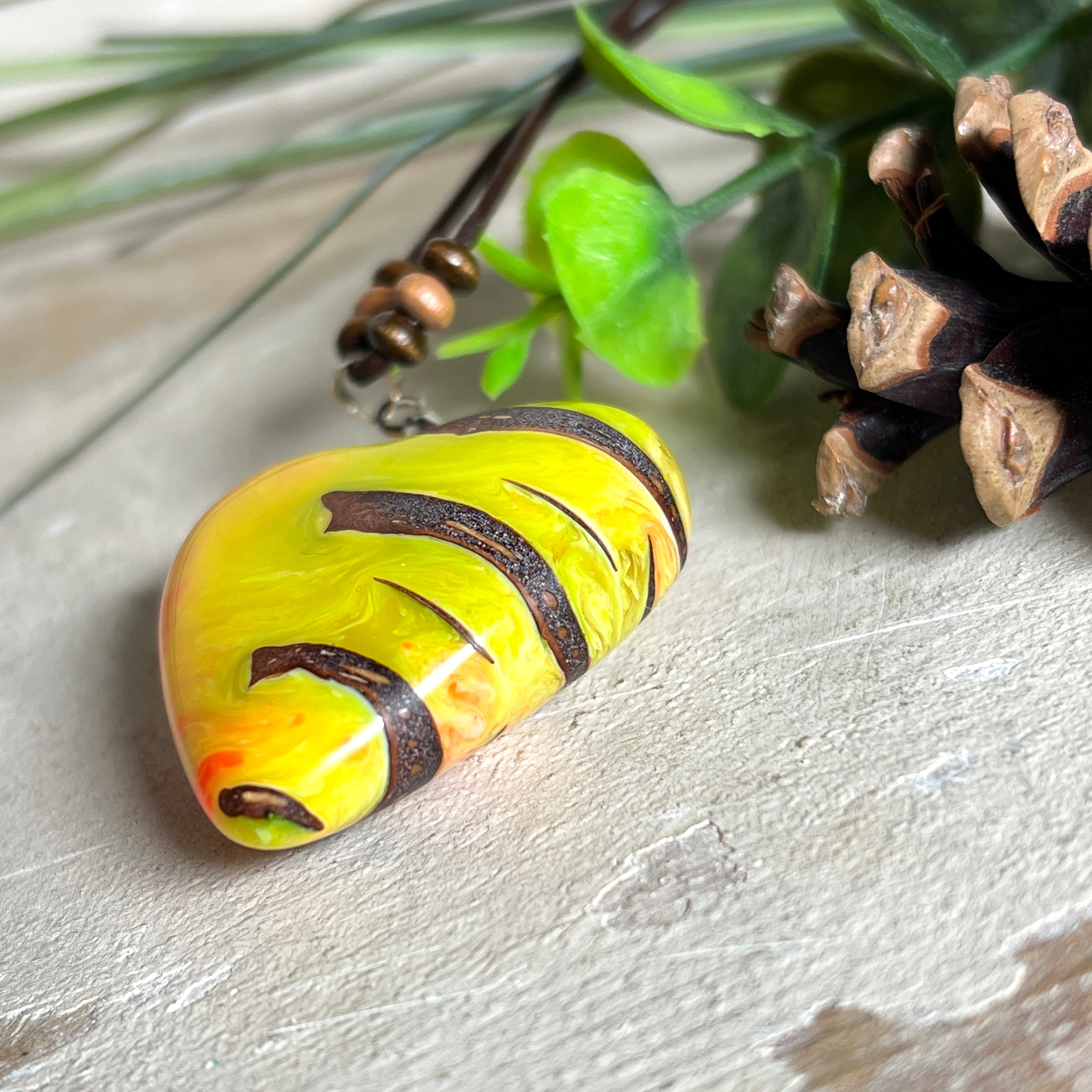 Herz-Anhänger aus Pinienzapfen & Harz, fluoreszierend bei Schwarzlicht. Farben Gelb-Orange-Weiß, Größe 4,2 × 3,8 cm. Lederband verstellbar.