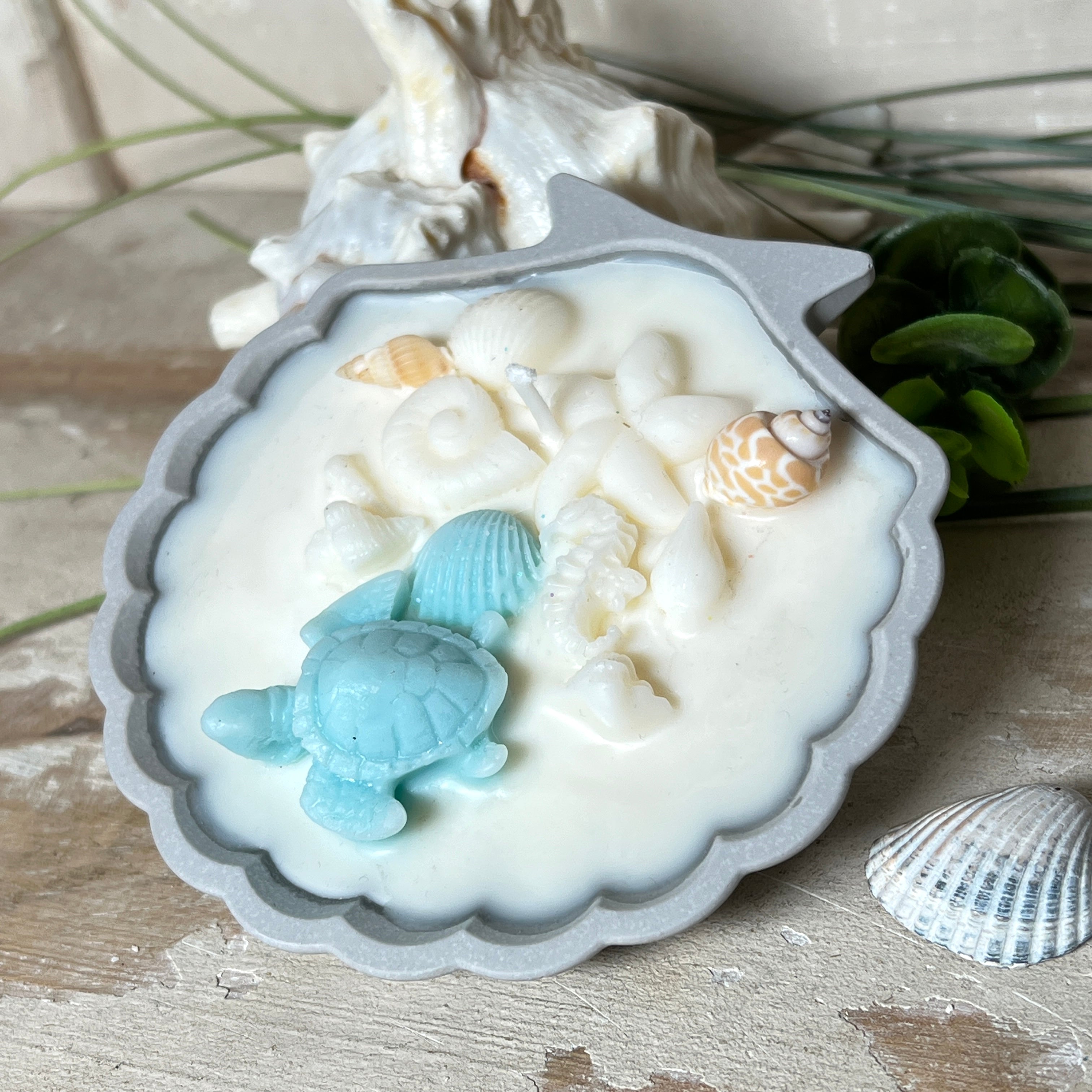 andgefertigte Kerze „Ozeanfreund“ in Jesmonite-Schale (ca. 11 cm). Gefüllt mit nachhaltigem Sojawachs, dekoriert mit echten Muscheln, handgegossenen Wachsmuscheln und einer türkisfarbenen Wachsschildkröte. Maritime Kerze – einzigartig, dekorativ und perfekt als Geschenk oder als Meeres-Deko.
