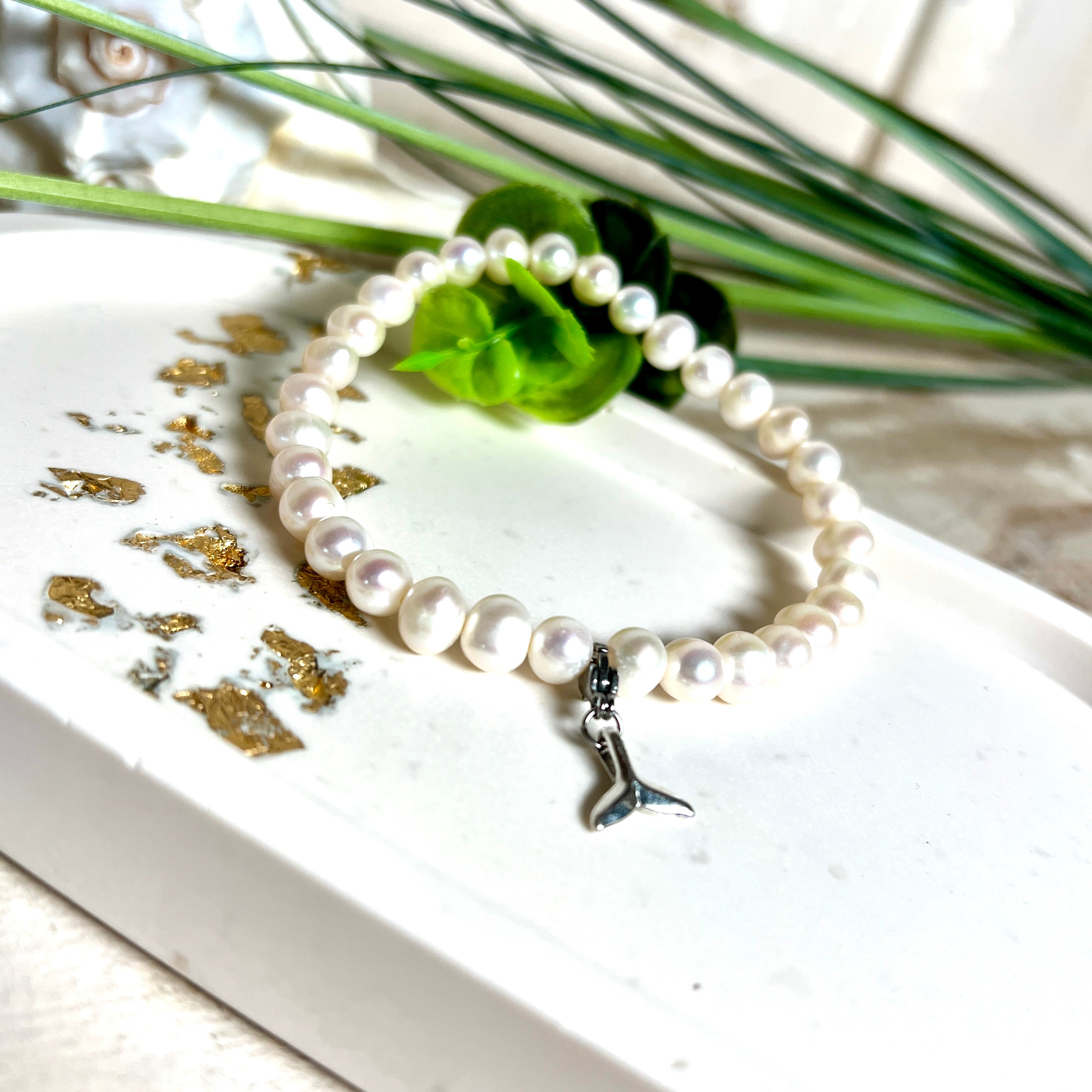Handgefertigtes Armband aus echten Süßwasserperlen (ca. 6-7 mm), elastisch aufgezogen mit einem Edelstahl-Charm in Form einer Walflosse. Maritimes Design mit Bedeutung – stilvoll, natürlich und elegant. Größe ca. 17,5 cm. Ideal als Geschenk für Meeresliebhaberinnen oder für sich selbst.