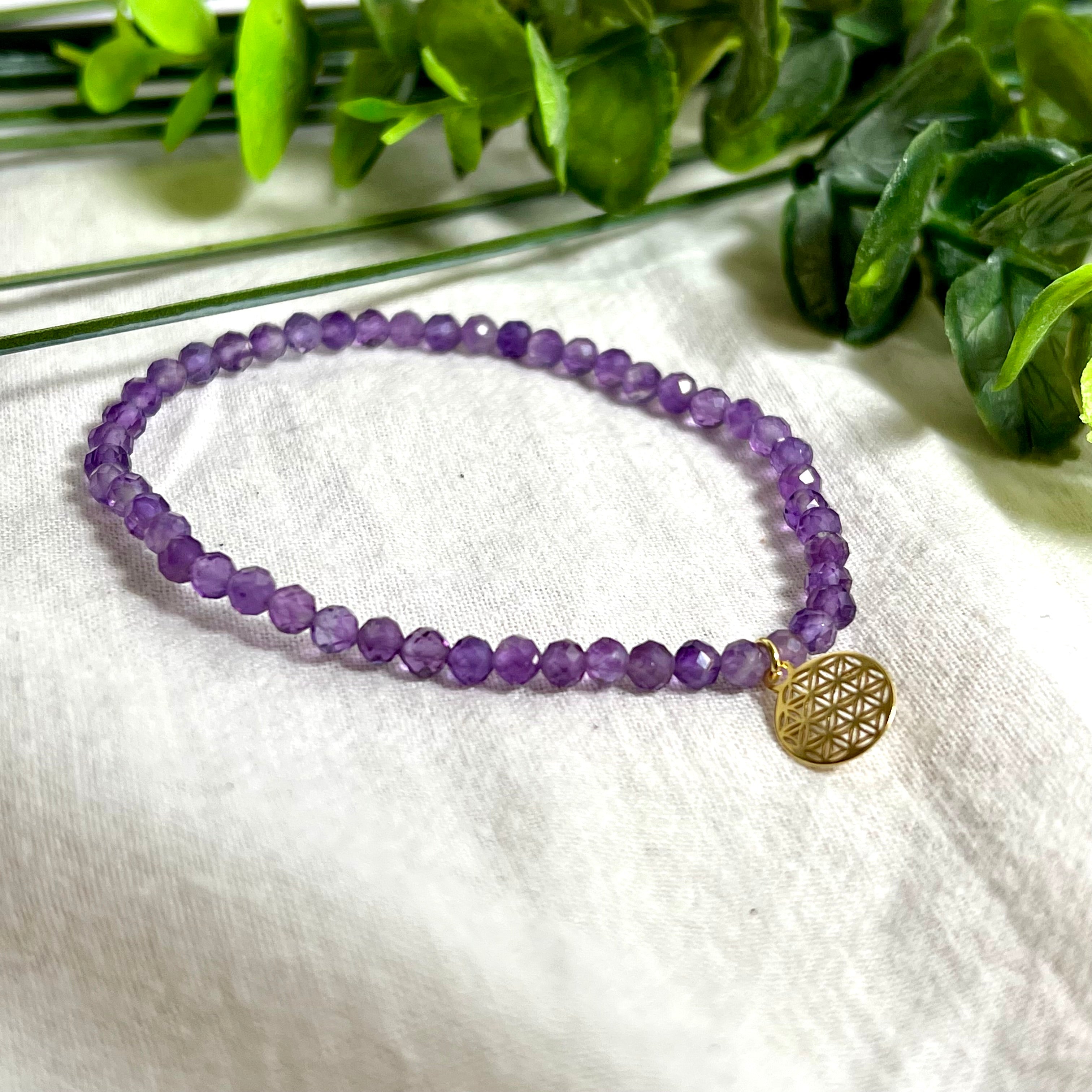 Handgefertigtes Amethyst-Armband mit facettierten 4 mm Edelstein-Perlen in zartem Violett, ergänzt durch einen vergoldeten 925 Silber Charm in Form der Blume des Lebens. Elastisches Design mit ca. 17 cm Innendurchmesser. Elegant, spirituell und fein – ein besonderes Schmuckstück für Achtsamkeit, Energie und Harmonie im Alltag.