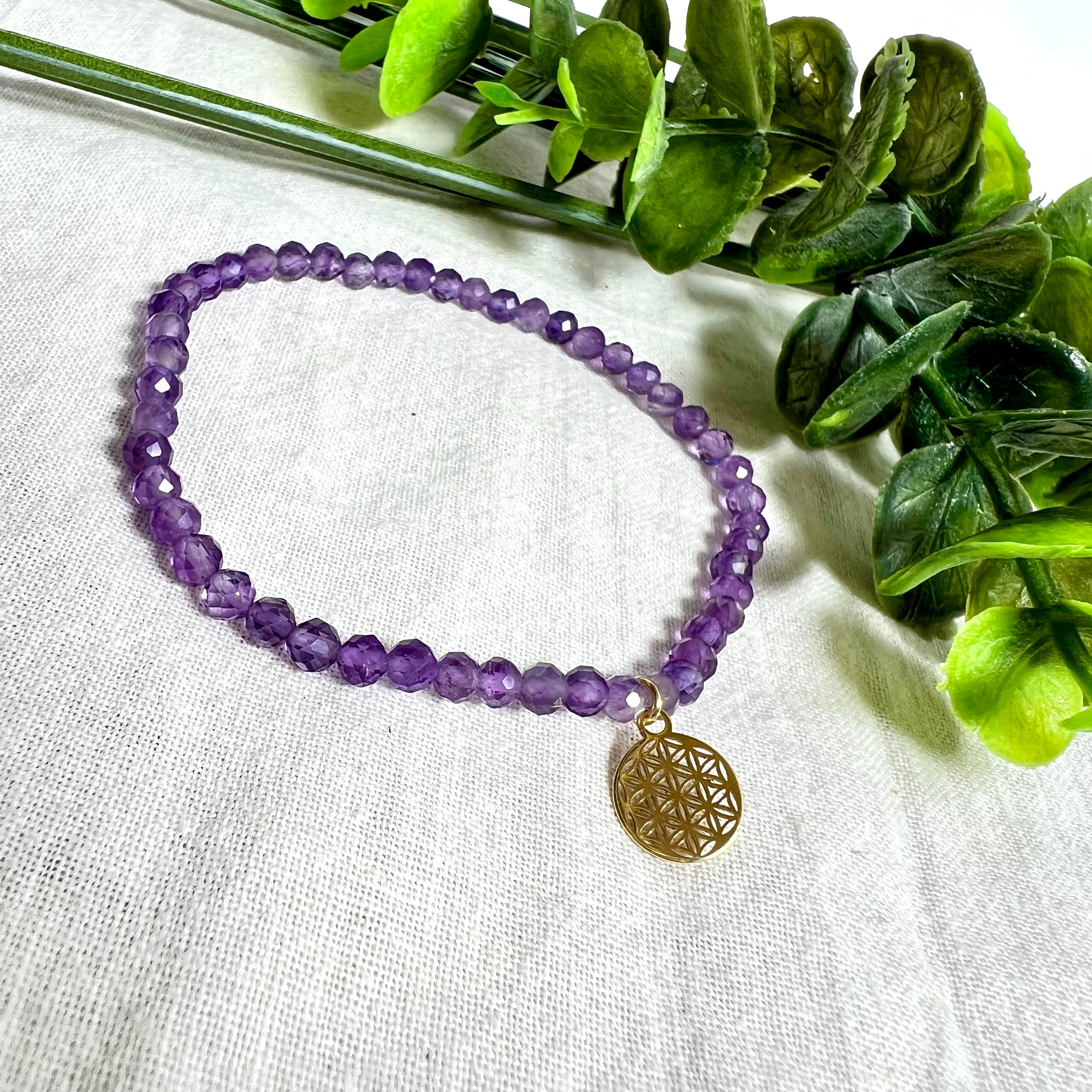 Handgefertigtes Amethyst-Armband mit facettierten 4 mm Edelstein-Perlen in zartem Violett, ergänzt durch einen vergoldeten 925 Silber Charm in Form der Blume des Lebens. Elastisches Design mit ca. 17 cm Innendurchmesser. Elegant, spirituell und fein – ein besonderes Schmuckstück für Achtsamkeit, Energie und Harmonie im Alltag.