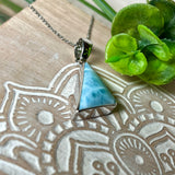 Larimar Anhänger in markanter Dreiecksform, eingefasst in rhodiniertes 925 Sterling Silber, vor strukturiertem Hintergrund mit grünen Blättern – stilvoller Edelsteinschmuck mit karibischem Flair.