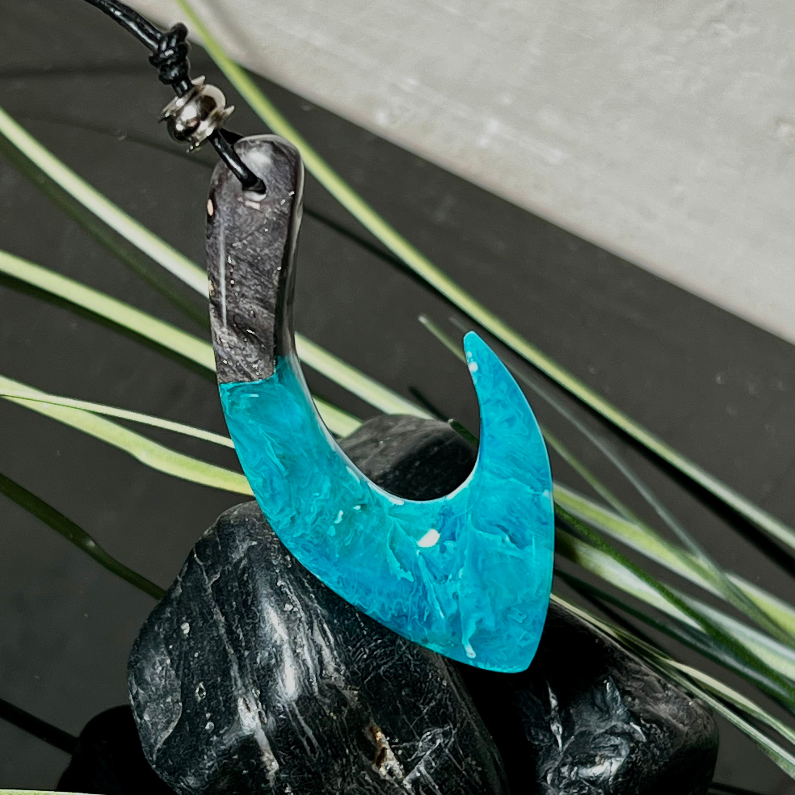 Handgefertigter Maori-Anhänger „Tangaroa Spirit“ in traditioneller Hakenform, gefertigt aus stabilisiertem Maserholz und ozeanblauem Harz. Die polierte Oberfläche bringt die natürlichen Maserungen und das tiefblaue Farbspiel besonders zur Geltung. Symbolisiert Schutz, Stärke und die Verbundenheit zum Meer. Verstellbares Lederband mit Schiebeknoten und dekorativen Holz- sowie Metallperlen – ideal als kraftvoller Talisman oder Geschenk.