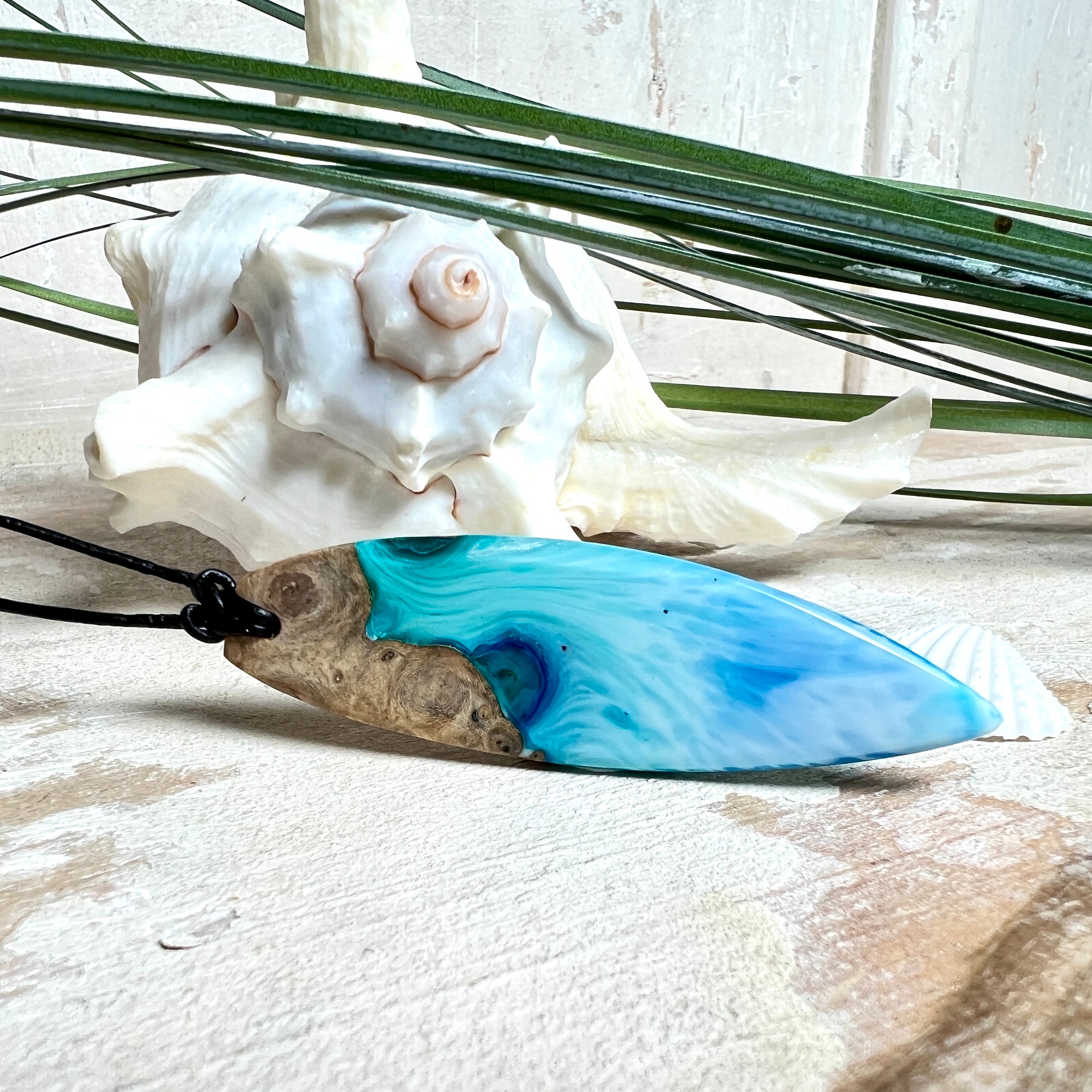 Surfbrett-Anhänger handgefertigt aus Maserholz & Harz in Blau-Weiß. Größe ca. 6,3 × 2 cm. Lederband verstellbar 26–47 cm, Schiebeknoten mit Holzperlen.