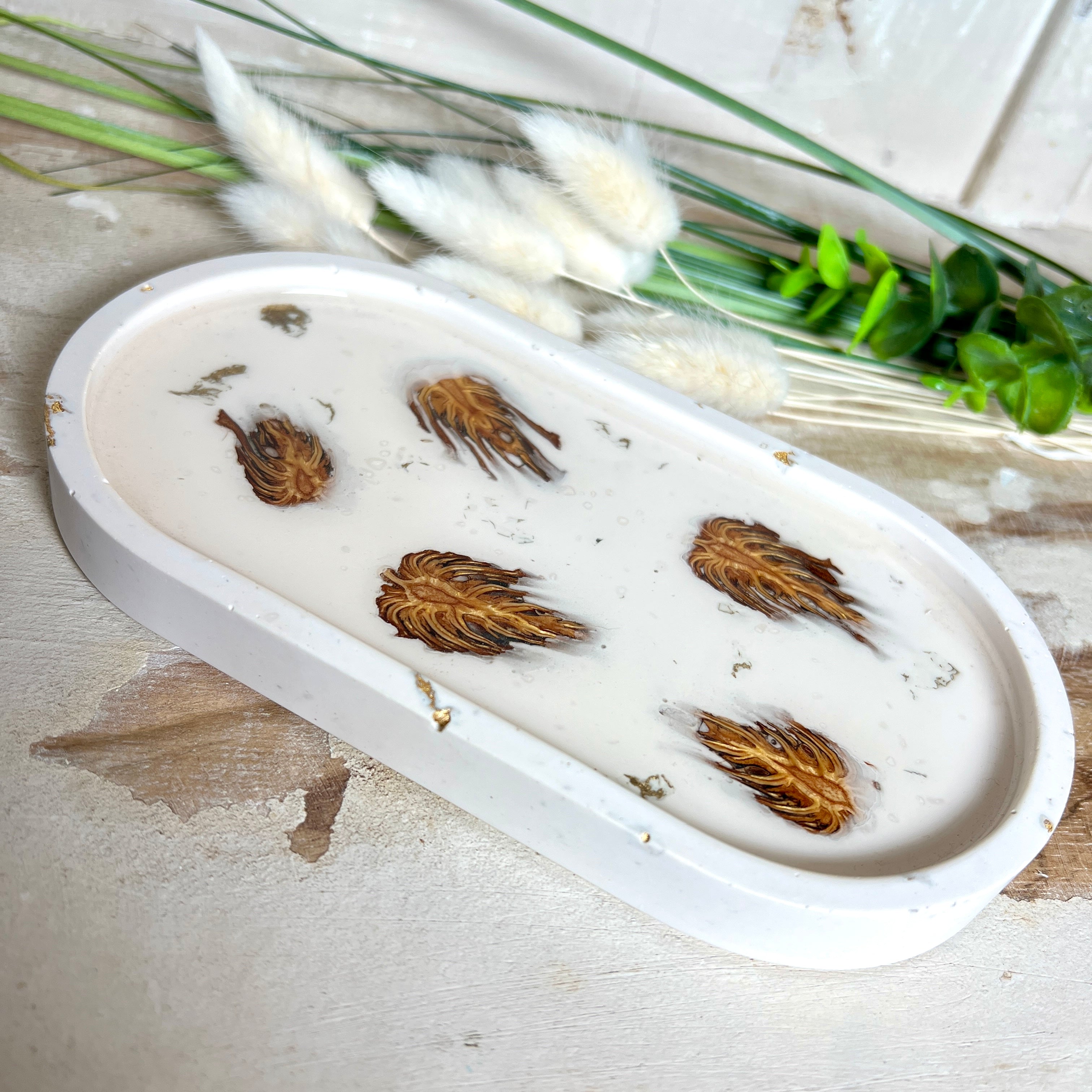 Handgefertigtes Schmucktablett aus Jesmonite mit echten Zapfen, die in einer glänzenden Resin-Schicht eingebettet sind. Die ovale Form und die natürliche Farbgebung machen es zu einem stilvollen Wohnaccessoire. Mit rutschfesten Korkpunkten auf der Unterseite ideal als Ablage für Schmuck, Schlüssel oder Dekoartikel. Jeder Artikel ist ein Unikat aus Handarbeit – Lieferung ohne Dekoration.