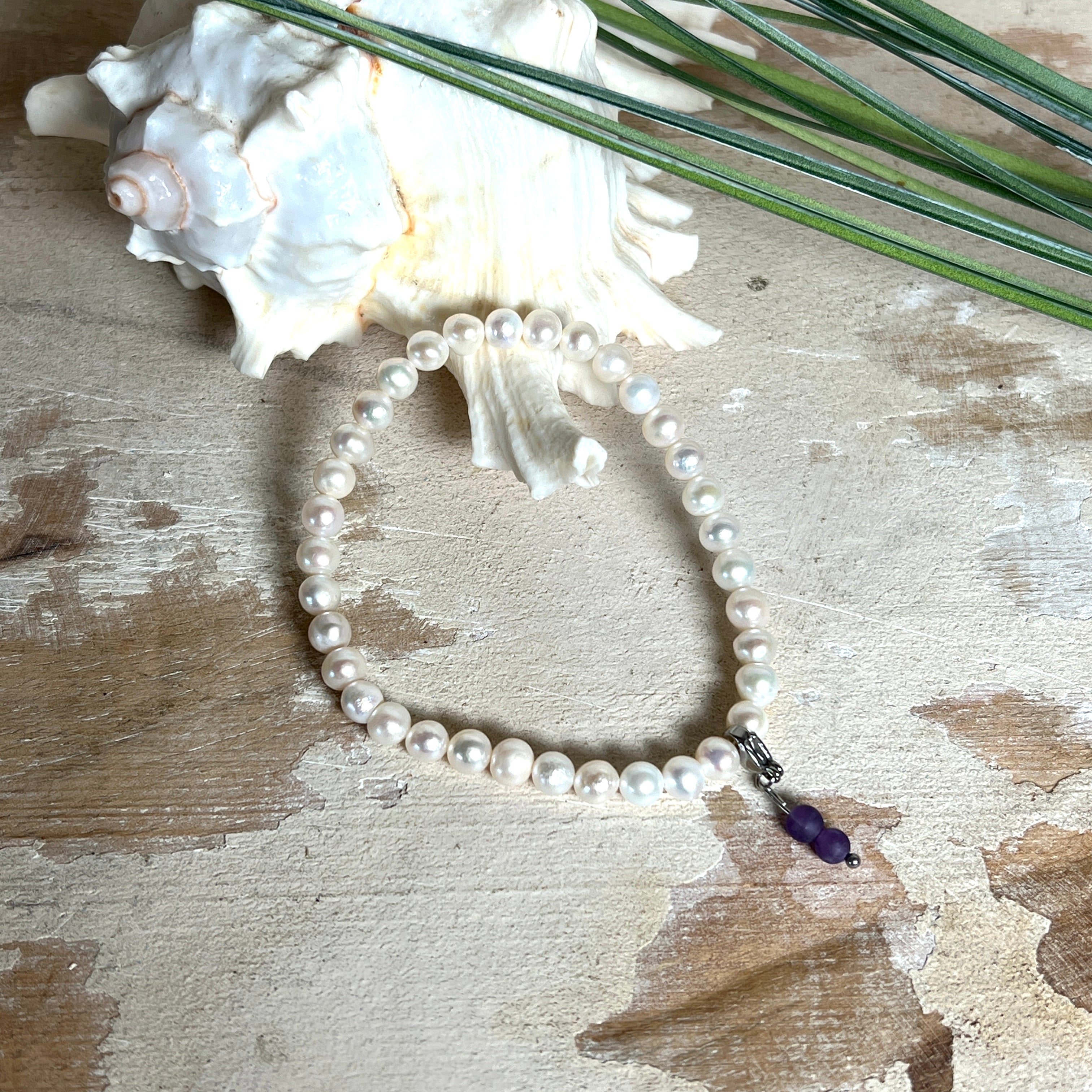 Handgefertigtes Armband „Sea Harmony“ mit schimmernden Süßwasserperlen (Ø ca. 6–7 mm), jede Perle ein Unikat. Auf elastischem Band gefädelt, mit einem filigranen Charmanhänger aus Amethyst-Perlen, befestigt an einem robusten Edelstahl-Karabiner. Ein Schmuckstück voller Eleganz, maritimer Harmonie und symbolischer Tiefe – ideal als Geschenk oder als stilvolles Accessoire.