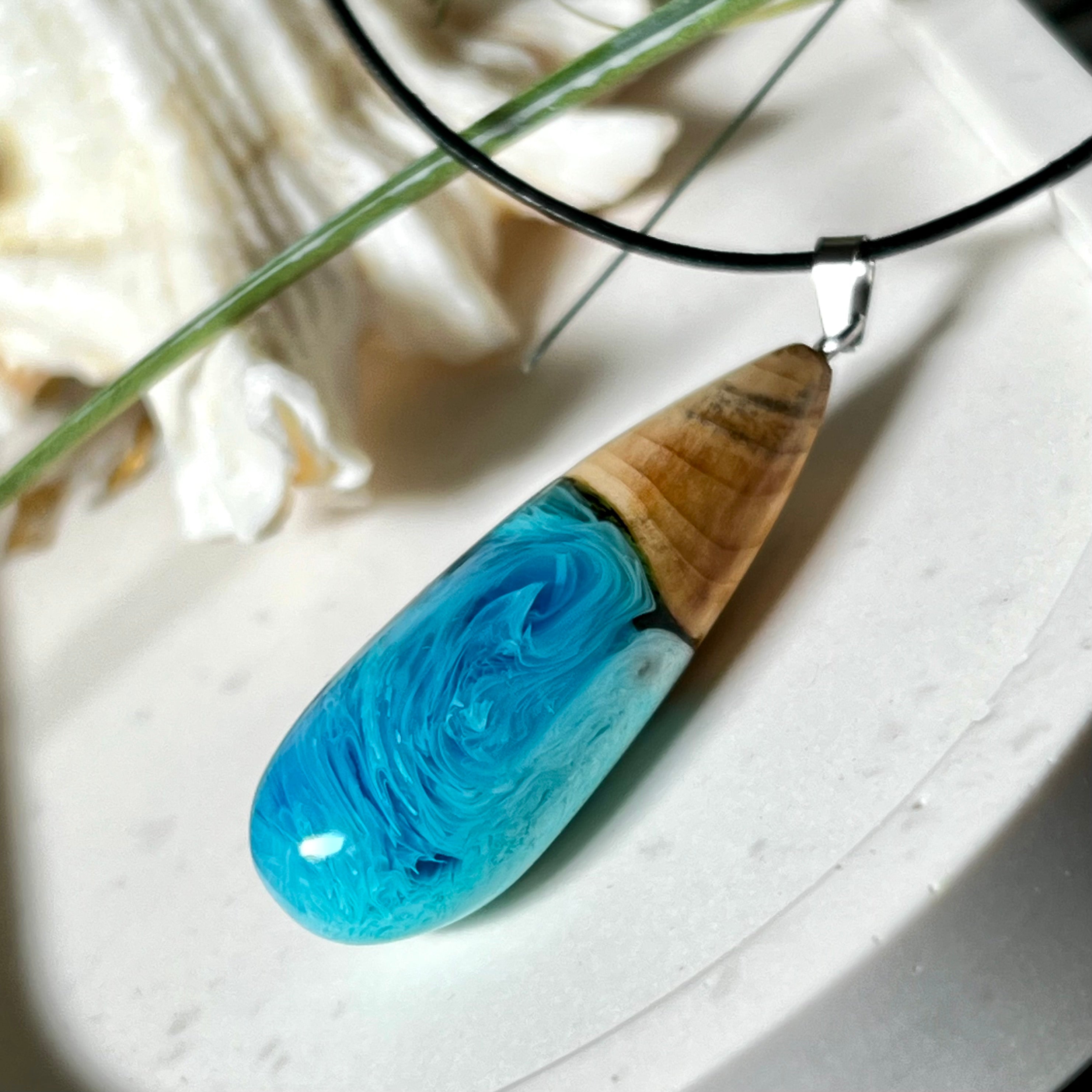 Tropfenförmiger Anhänger aus Maserholz und Harz in leuchtenden Blautönen und Weiß. Inspiriert vom Meer, in Handarbeit gegossen,gesägt, geschliffen und hochglanzpoliert. Mit verstellbarer Lederkette (45 + 5 cm) und Edelstahlkarabiner. Jeder Anhänger ist ein Unikat mit natürlicher Maserung. Ein maritimes Schmuckstück für Naturfreunde und alle, die das Wasser lieben.