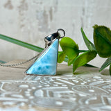 Larimar Anhänger in markanter Dreiecksform, eingefasst in rhodiniertes 925 Sterling Silber, vor strukturiertem Hintergrund mit grünen Blättern – stilvoller Edelsteinschmuck mit karibischem Flair.