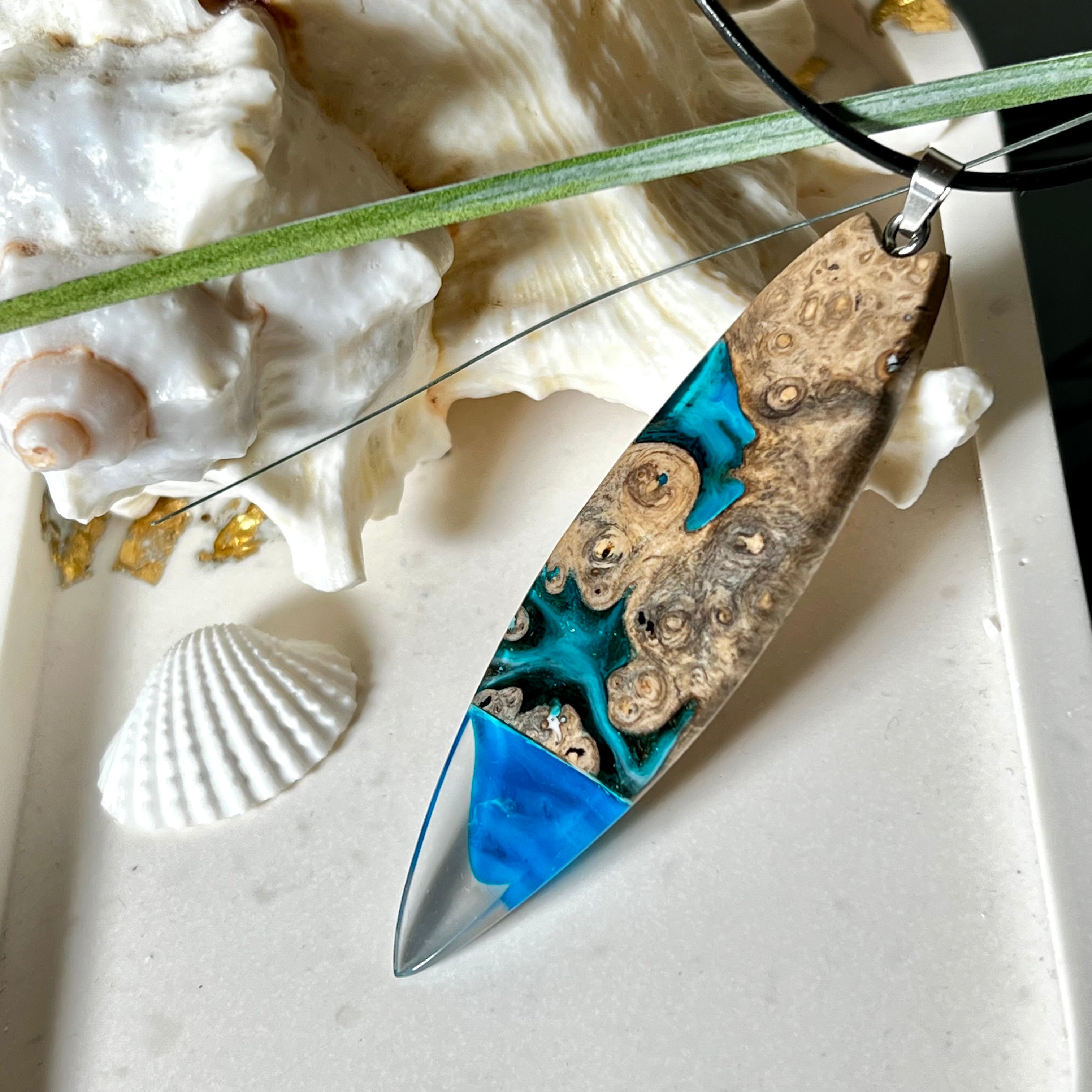 Handgefertigter Surfbrett-Anhänger aus Maserholz und transparentem Harz mit Farbverlauf in Blau und Weiß. Die natürliche Maserung des Holzes trifft auf ozeanartige Harzstrukturen. Größe ca. 6,7 x 2 cm, mit Edelstahlöse und Lederband inkl. Karabinerverschluss (45 cm + 5 cm Verlängerung). Jedes Stück ist ein Unikat – maritim, modern und mit viel Liebe gefertigt.