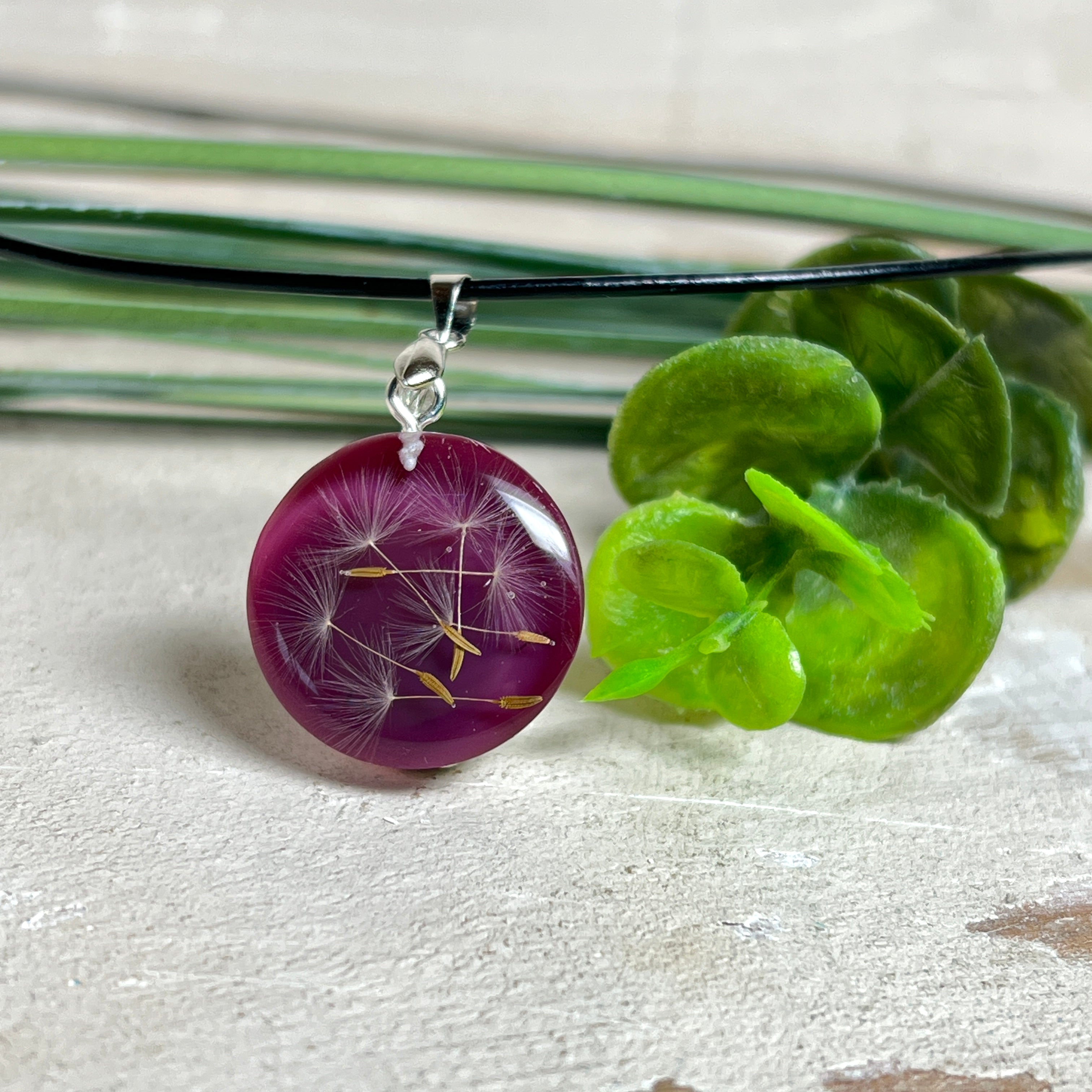 Runder Pusteblumen-Anhänger aus Harz, Hintergrund Brombeerfarben. Durchmesser 22 mm, Edelstahlöse, Lederkette verstellbar mit Edelstahlverschluss.