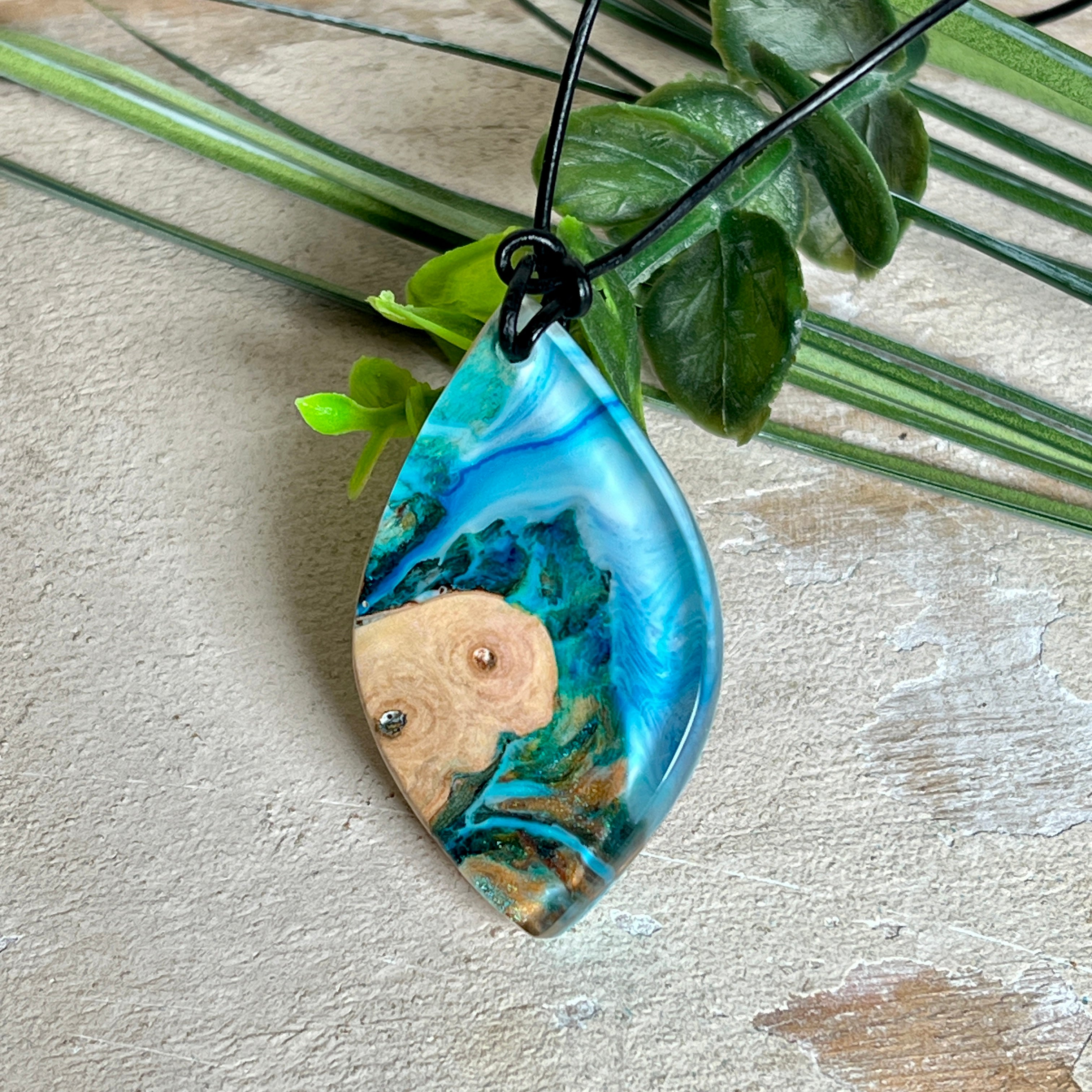 Handgefertigter Anhänger „Ocean Leaf“ aus Maserholz und Epoxidharz in Blau- und Türkistönen. Ein einzigartiges Schmuckstück, das die Schönheit von Natur und Meer einfängt. Mit verstellbarem Lederband (24–43 cm). Jeder Anhänger ist ein Unikat mit einzigartiger Maserung und Farbverlauf.
