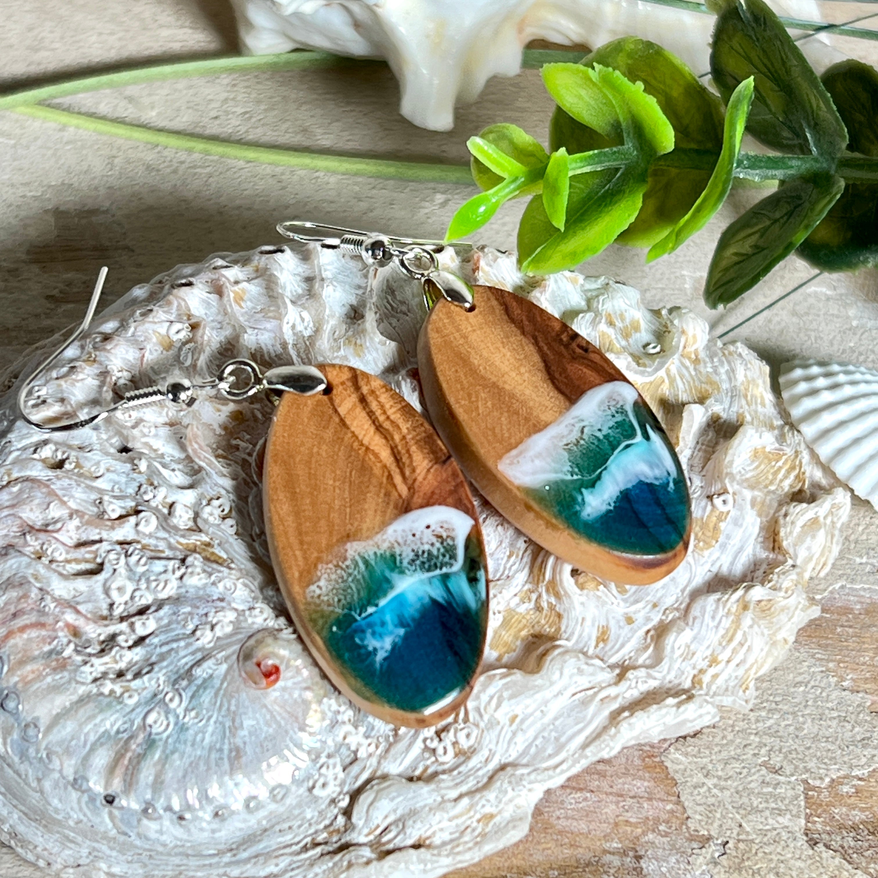 Handgefertigte Ohrringe „Wave Harmony“ aus Olivenholz und Epoxidharz in Blau-, Türkis- und Weißtönen. Das Design erinnert an Meereswellen am Strand. Jeder Ohrring ist ein Unikat mit individueller Maserung. Versilberte, nickelfreie und bleifreie Anhängerschlaufe, 925 Silber Ohrhaken. Maritimer Schmuck – perfekt für Meerliebhaber und als edles Geschenk.