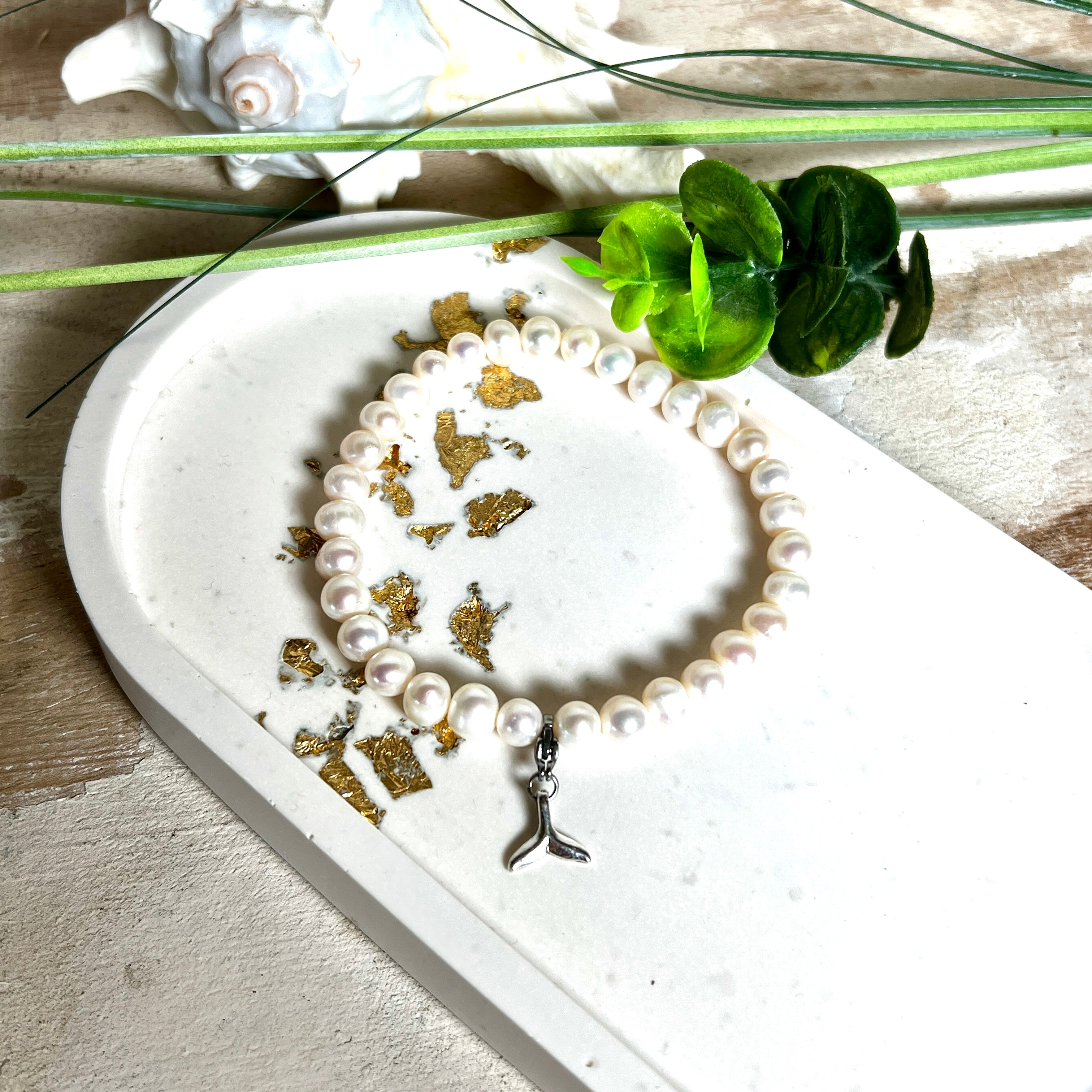 Handgefertigtes Armband aus echten Süßwasserperlen (ca. 6-7 mm), elastisch aufgezogen mit einem Edelstahl-Charm in Form einer Walflosse. Maritimes Design mit Bedeutung – stilvoll, natürlich und elegant. Größe ca. 17,5 cm. Ideal als Geschenk für Meeresliebhaberinnen oder für sich selbst.