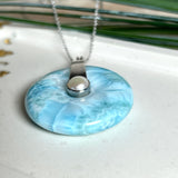 Echter Larimar-Donut (42 mm) mit Süßwasserperle, gefasst in rhodiniertem 925 Sterlingsilber. Mit 45 cm langer, rhodinierter Silberkette. Selten, edel & handgefertigt – inspiriert vom Blau der Karibik.