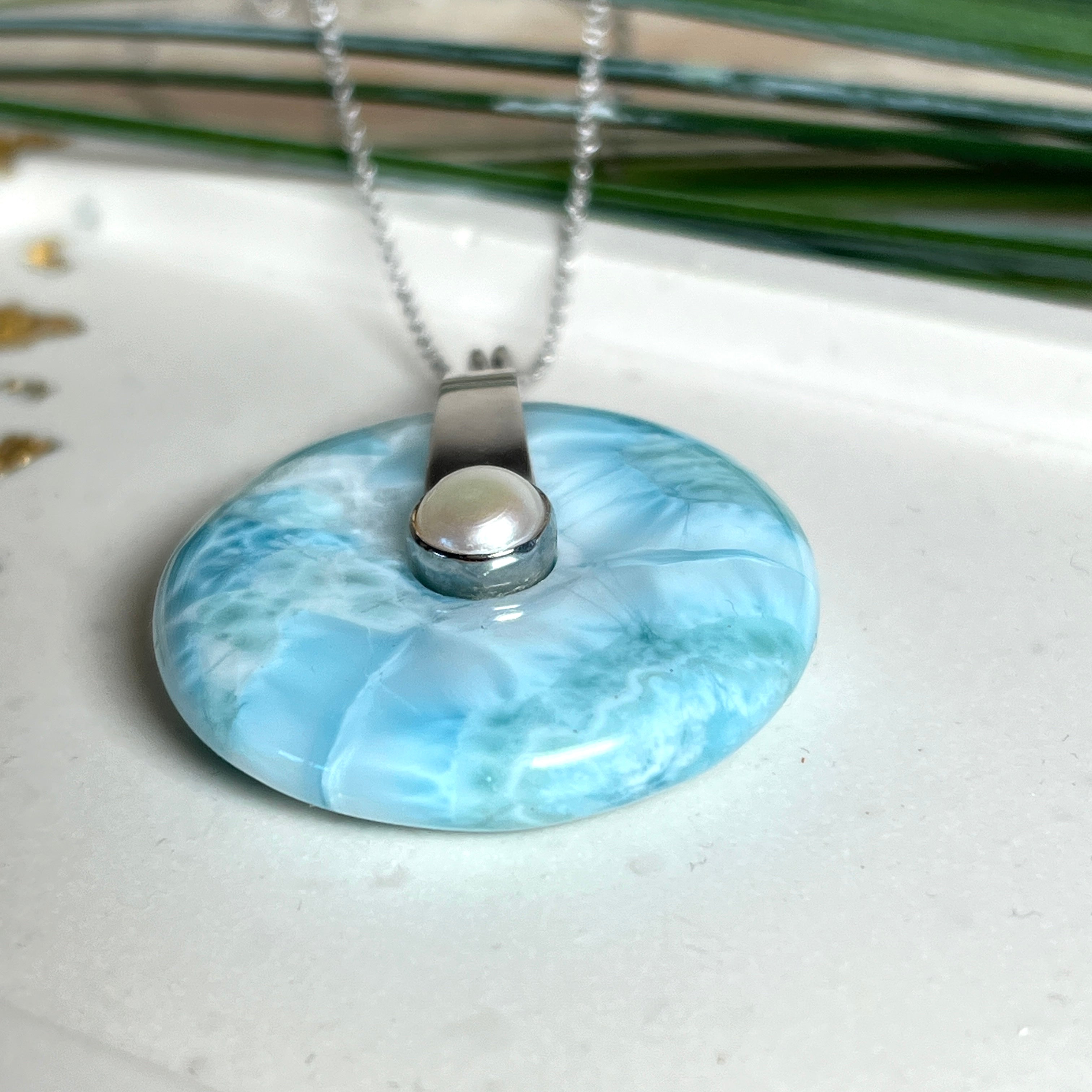 Echter Larimar-Donut (42 mm) mit Süßwasserperle, gefasst in rhodiniertem 925 Sterlingsilber. Mit 45 cm langer, rhodinierter Silberkette. Selten, edel & handgefertigt – inspiriert vom Blau der Karibik.