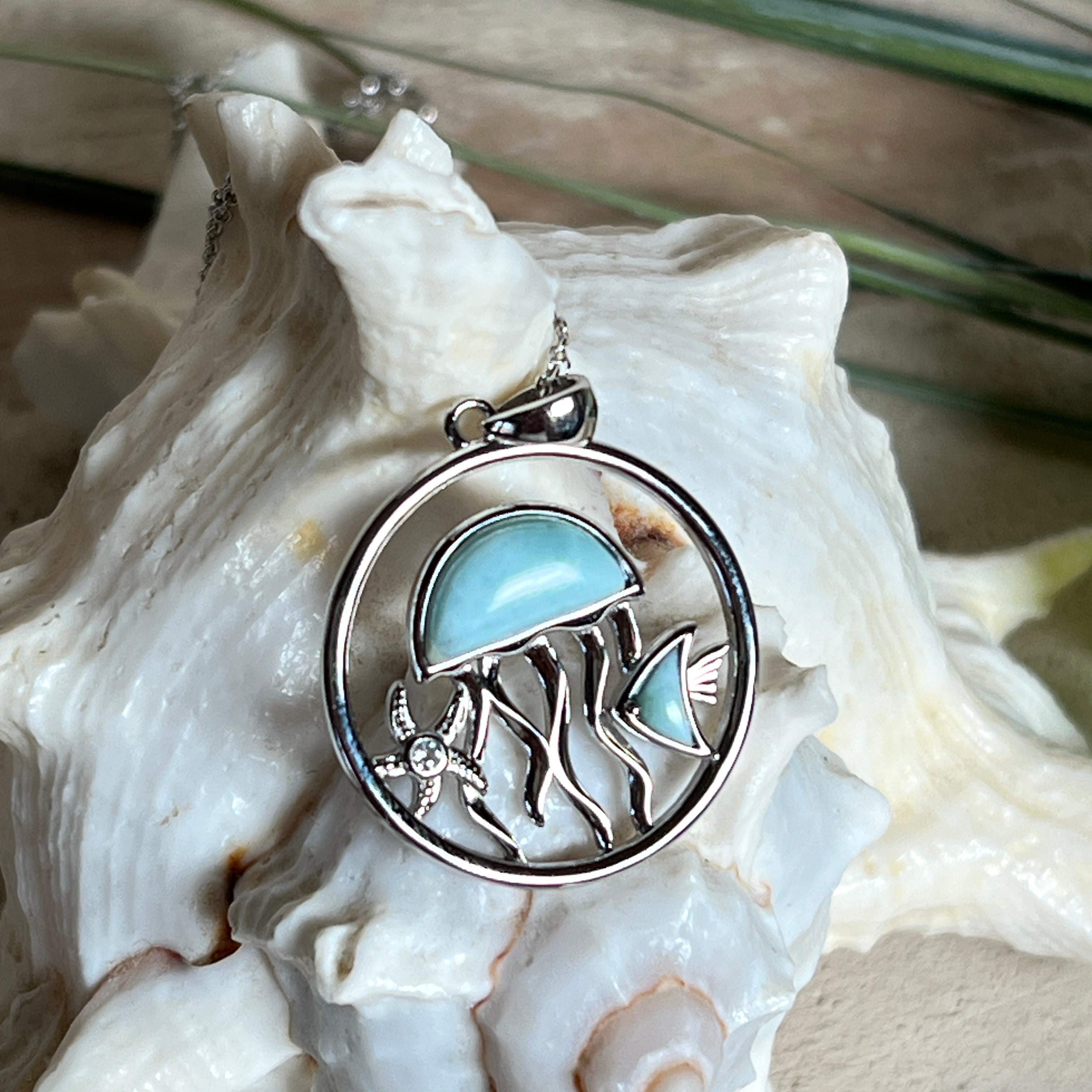 „Sealife“ – runder Anhänger aus rhodiniertem 925 Sterling Silber mit seltenem Larimar und funkelndem Topas. Das maritime Design zeigt eine Qualle, einen Fisch und einen Seestern. Anhängergröße ca. 32 × 26 mm, inklusive 45 cm langer Silberkette (1 mm Stärke). Symbol für die Schönheit und Vielfalt des Ozeans – jedes Stück ein Unikat durch das natürliche Farbspiel des Larimars.