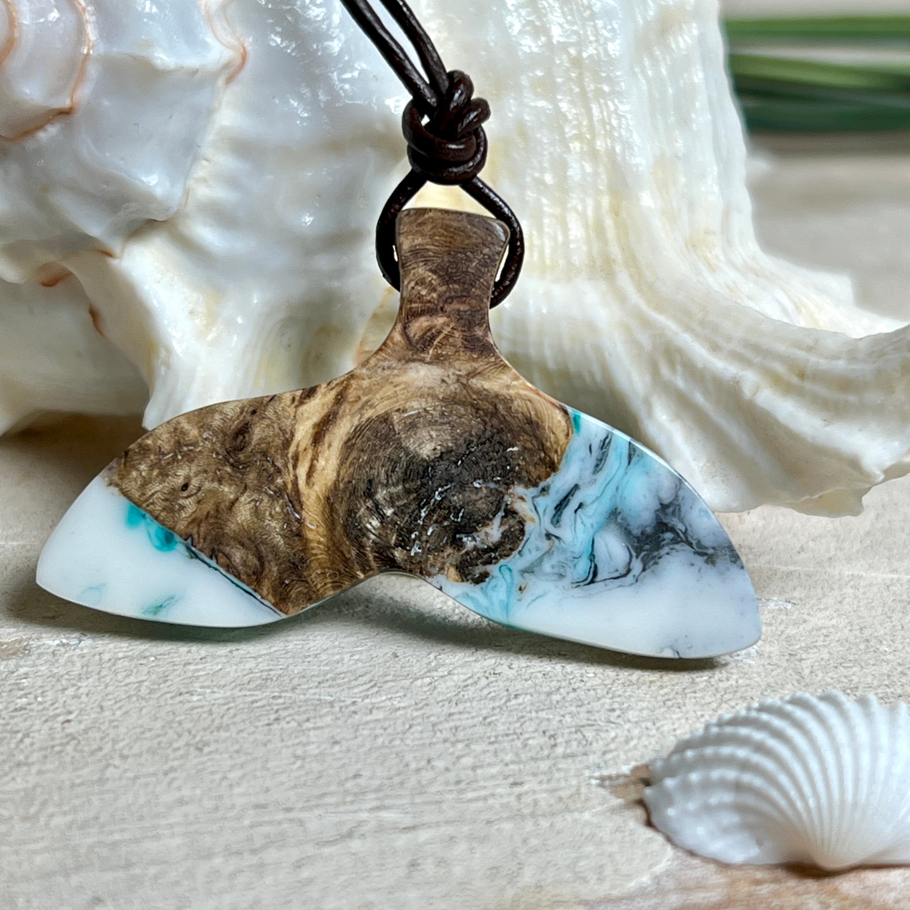 Walflossen-Anhänger „Flossenklang“ – handgefertigtes Unikat aus Maserholz und türkis-blau-grauen und weißem Harz. Die elegant geschwungene Form erinnert an die Flosse eines Wals und symbolisiert Freiheit, Stärke und Naturverbundenheit. Mit verstellbarem braunem Lederband gefertigt, ist jedes Stück ein individuelles Schmuckstück für Meeresliebhaber und Natursuchende. Maritimer Halsschmuck, inspiriert vom Ozean, glatt poliert und mit Liebe zum Detail von Hand gearbeitet.
