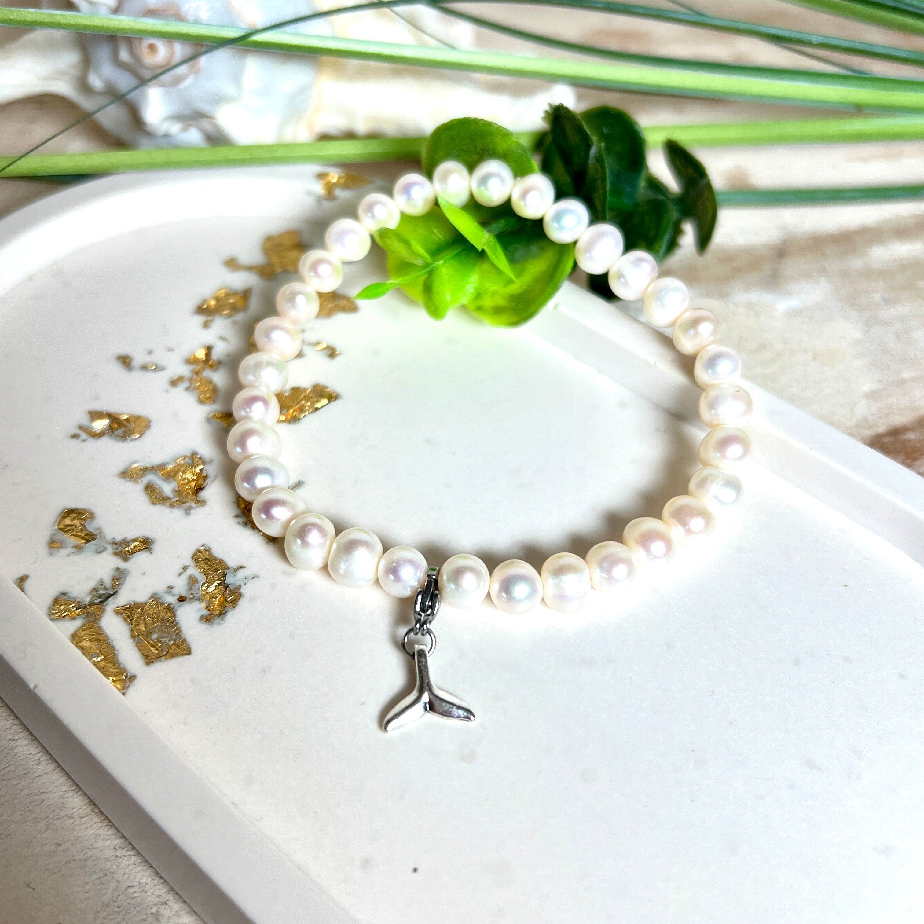 Handgefertigtes Armband aus echten Süßwasserperlen (ca. 6-7 mm), elastisch aufgezogen mit einem Edelstahl-Charm in Form einer Walflosse. Maritimes Design mit Bedeutung – stilvoll, natürlich und elegant. Größe ca. 17,5 cm. Ideal als Geschenk für Meeresliebhaberinnen oder für sich selbst.