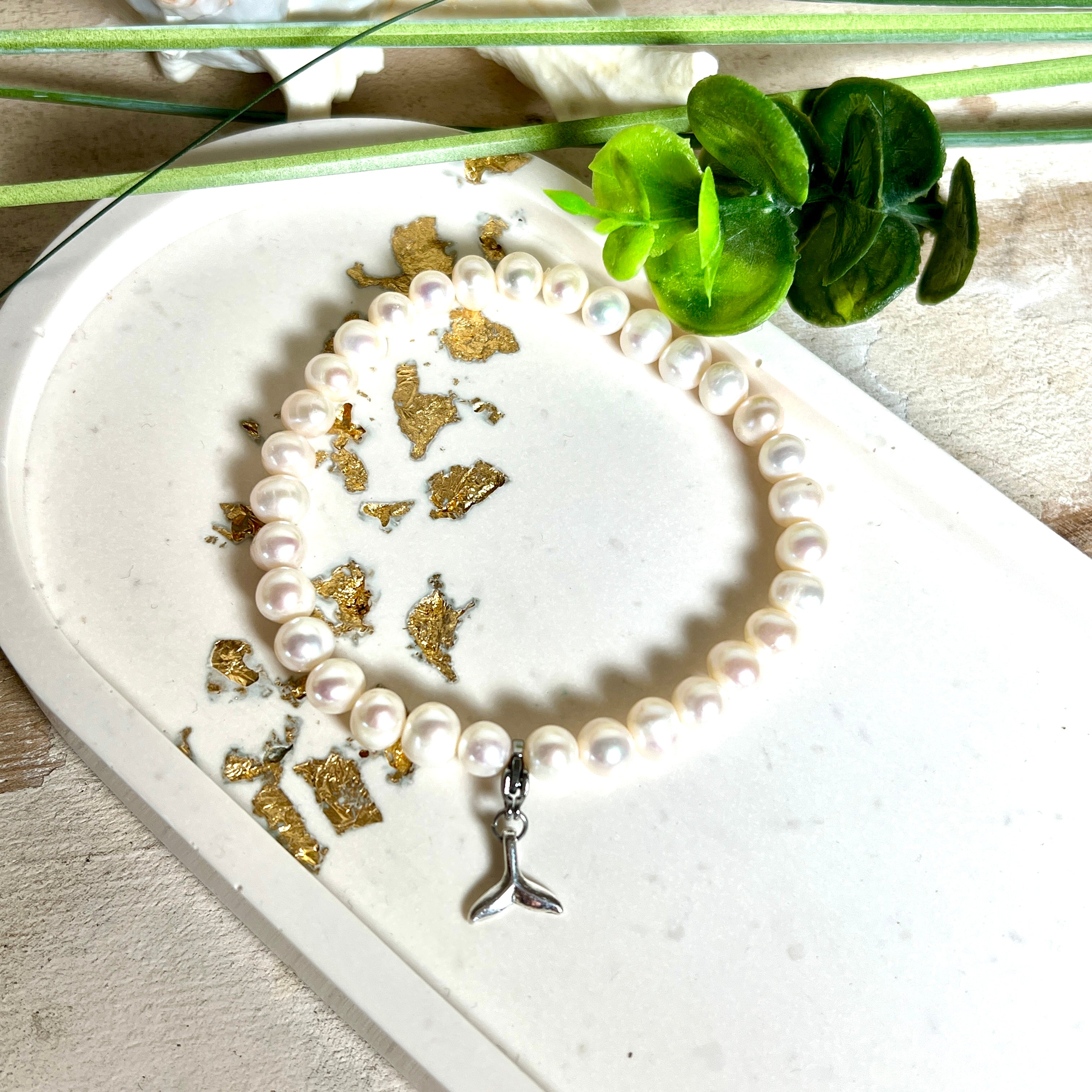 Handgefertigtes Armband aus echten Süßwasserperlen (ca. 6-7 mm), elastisch aufgezogen mit einem Edelstahl-Charm in Form einer Walflosse. Maritimes Design mit Bedeutung – stilvoll, natürlich und elegant. Größe ca. 17,5 cm. Ideal als Geschenk für Meeresliebhaberinnen oder für sich selbst.