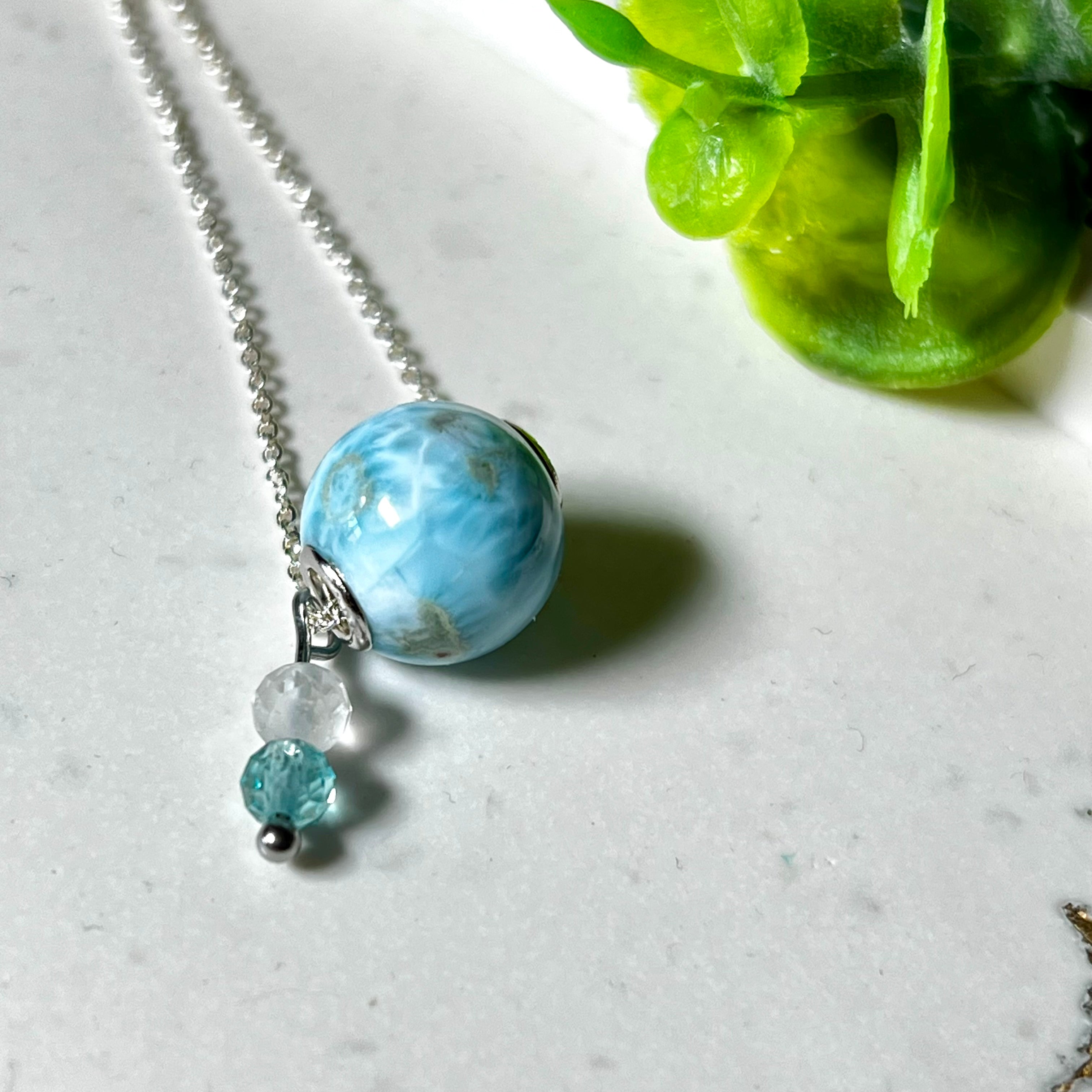 Feine Halskette aus 925er Silber mit einer polierten Larimar-Perle als Hauptstein, ergänzt durch funkelnde Apatit- und Bergkristall-Perlen. Der Edelstein mit seiner typischen Meeresfärbung erinnert an tropische Lagunen und steht für innere Ruhe und Klarheit.Ideal als Geschenk zum Geburtstag, für Meerliebhaber oder spirituelle Schmuckträgerinnen.