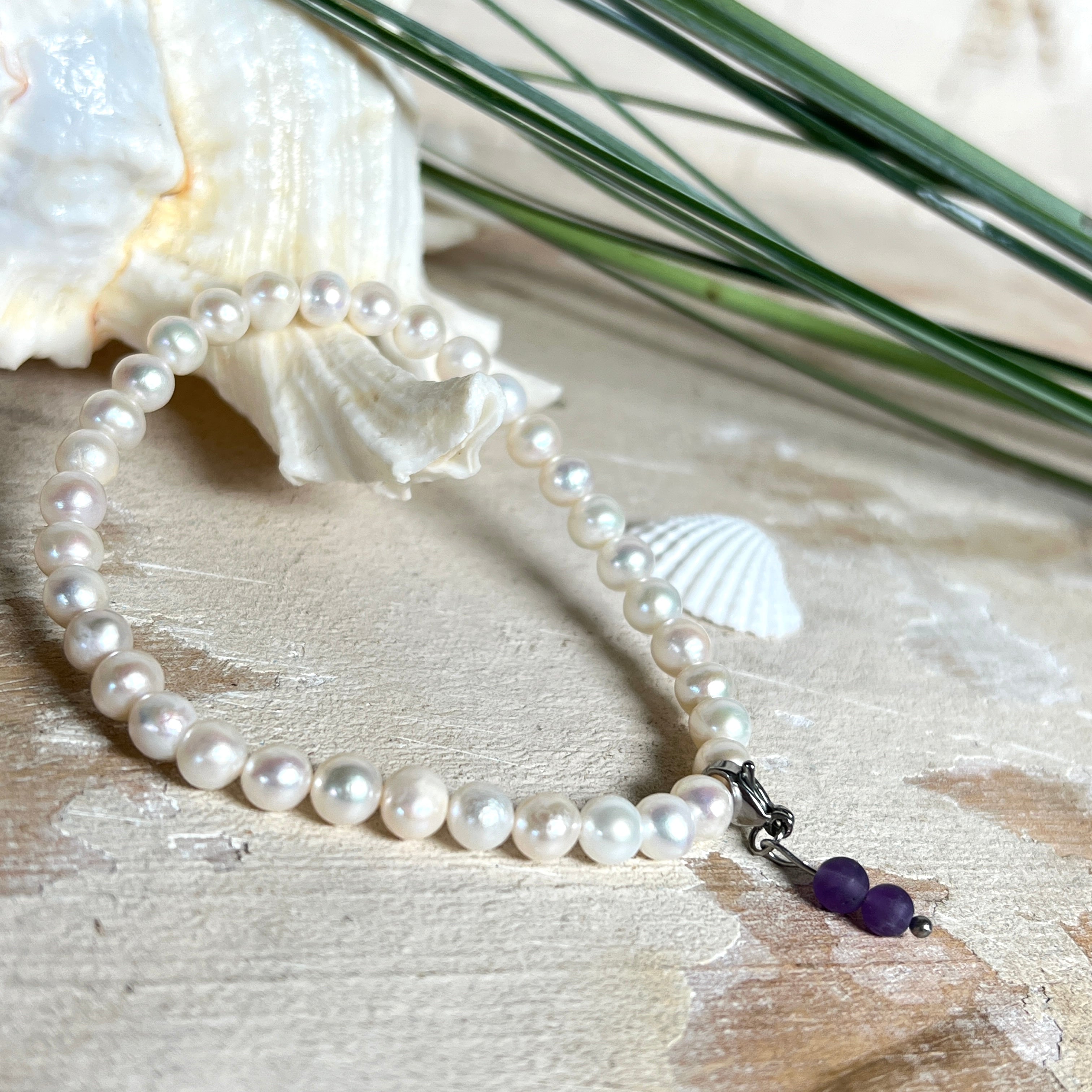 Handgefertigtes Armband „Sea Harmony“ mit schimmernden Süßwasserperlen (Ø ca. 6–7 mm), jede Perle ein Unikat. Auf elastischem Band gefädelt, mit einem filigranen Charmanhänger aus Amethyst-Perlen, befestigt an einem robusten Edelstahl-Karabiner. Ein Schmuckstück voller Eleganz, maritimer Harmonie und symbolischer Tiefe – ideal als Geschenk oder als stilvolles Accessoire.