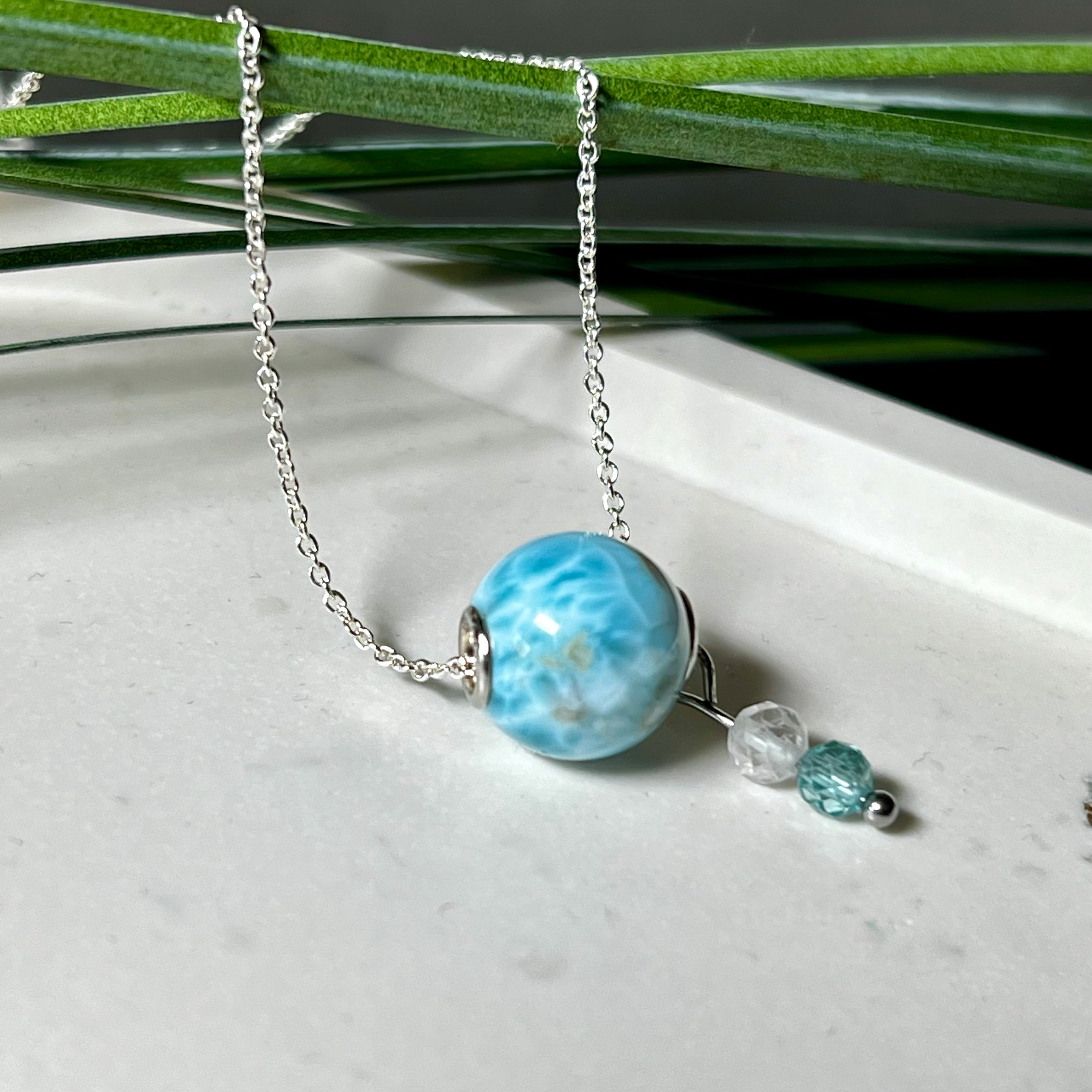 Feine Halskette aus 925er Silber mit einer polierten Larimar-Perle als Hauptstein, ergänzt durch funkelnde Apatit- und Bergkristall-Perlen. Der Edelstein mit seiner typischen Meeresfärbung erinnert an tropische Lagunen und steht für innere Ruhe und Klarheit.Ideal als Geschenk zum Geburtstag, für Meerliebhaber oder spirituelle Schmuckträgerinnen.