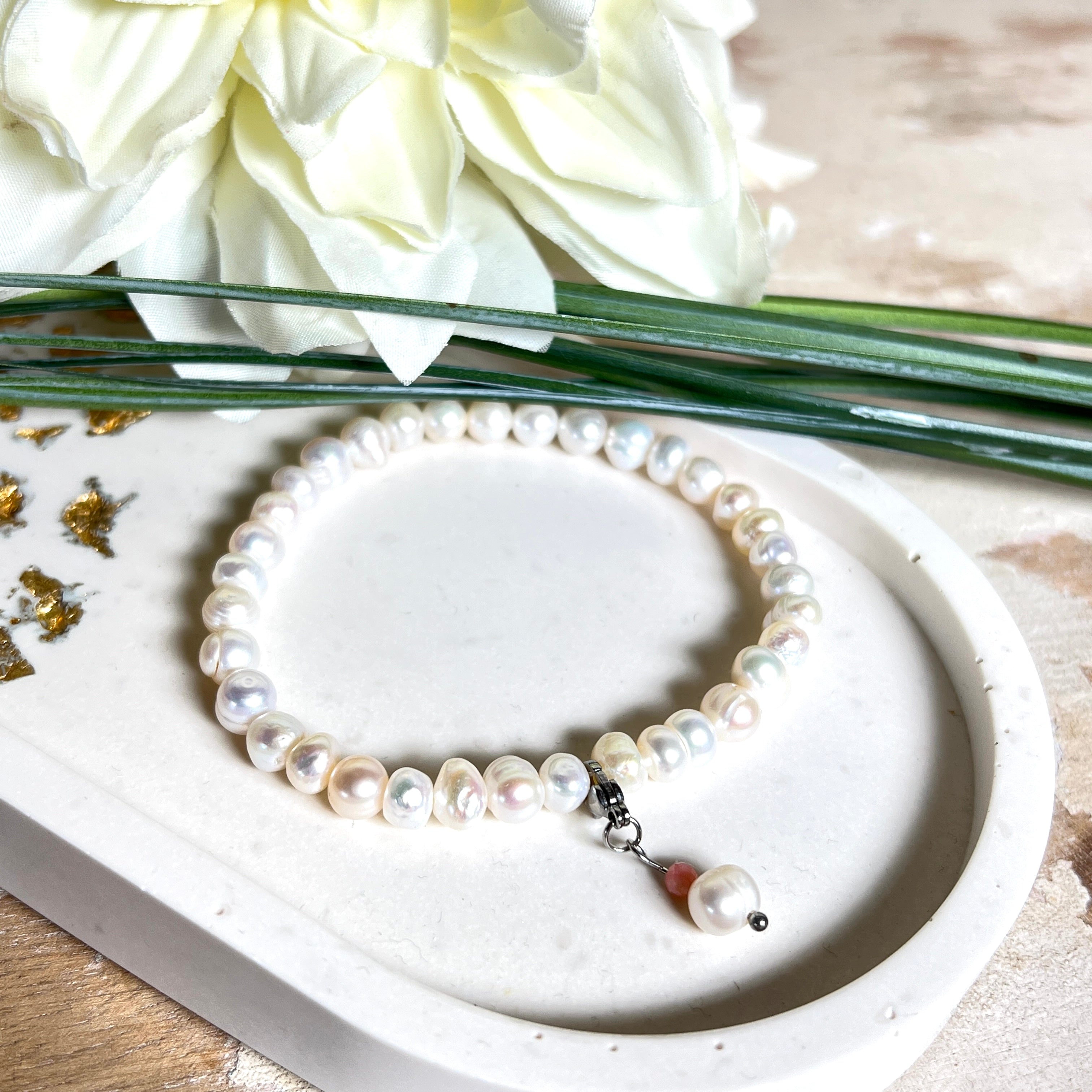 Handgefertigtes Armband „Ocean Bloom“ mit echten, schimmernden Süßwasserperlen (Ø ca. 6–7 mm) auf elastischem Band. Jede Perle ist ein Unikat mit natürlicher Form und sanftem Glanz. Highlight: Charmanhänger mit einer Süßwasserperle und einer facettierten Andenopal-Perle, befestigt an einem robusten Edelstahl-Karabiner. Ein Schmuckstück voller Eleganz, Symbolkraft und maritimer Schönheit.
