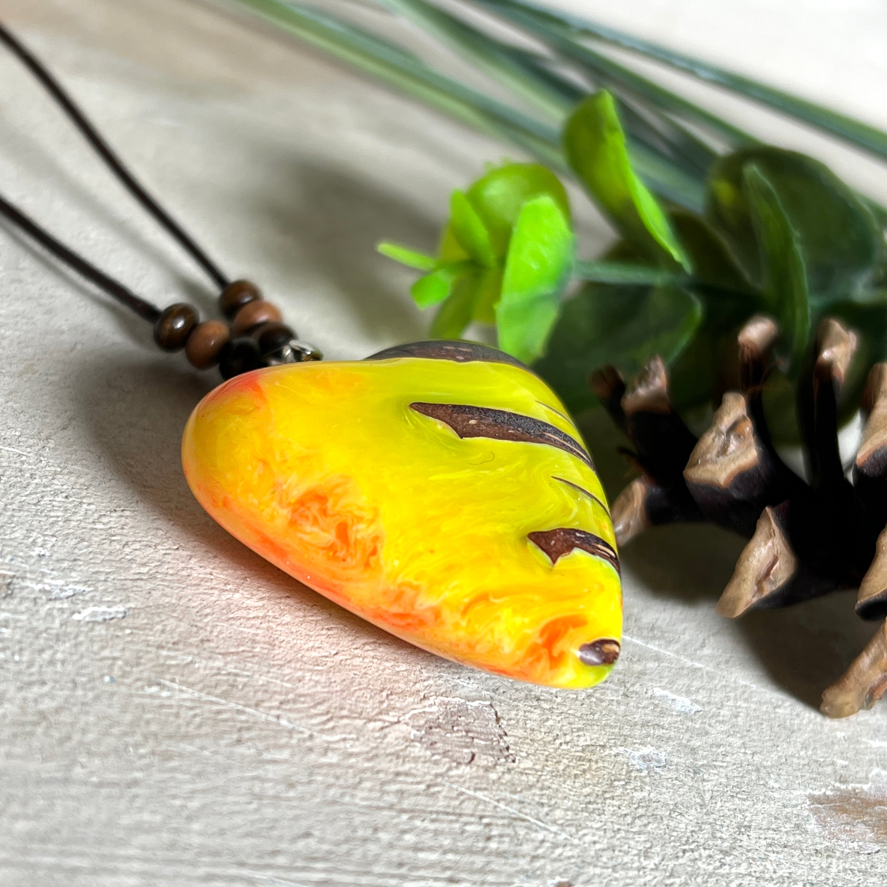 Herz-Anhänger aus Pinienzapfen & Harz, fluoreszierend bei Schwarzlicht. Farben Gelb-Orange-Weiß, Größe 4,2 × 3,8 cm. Lederband verstellbar.