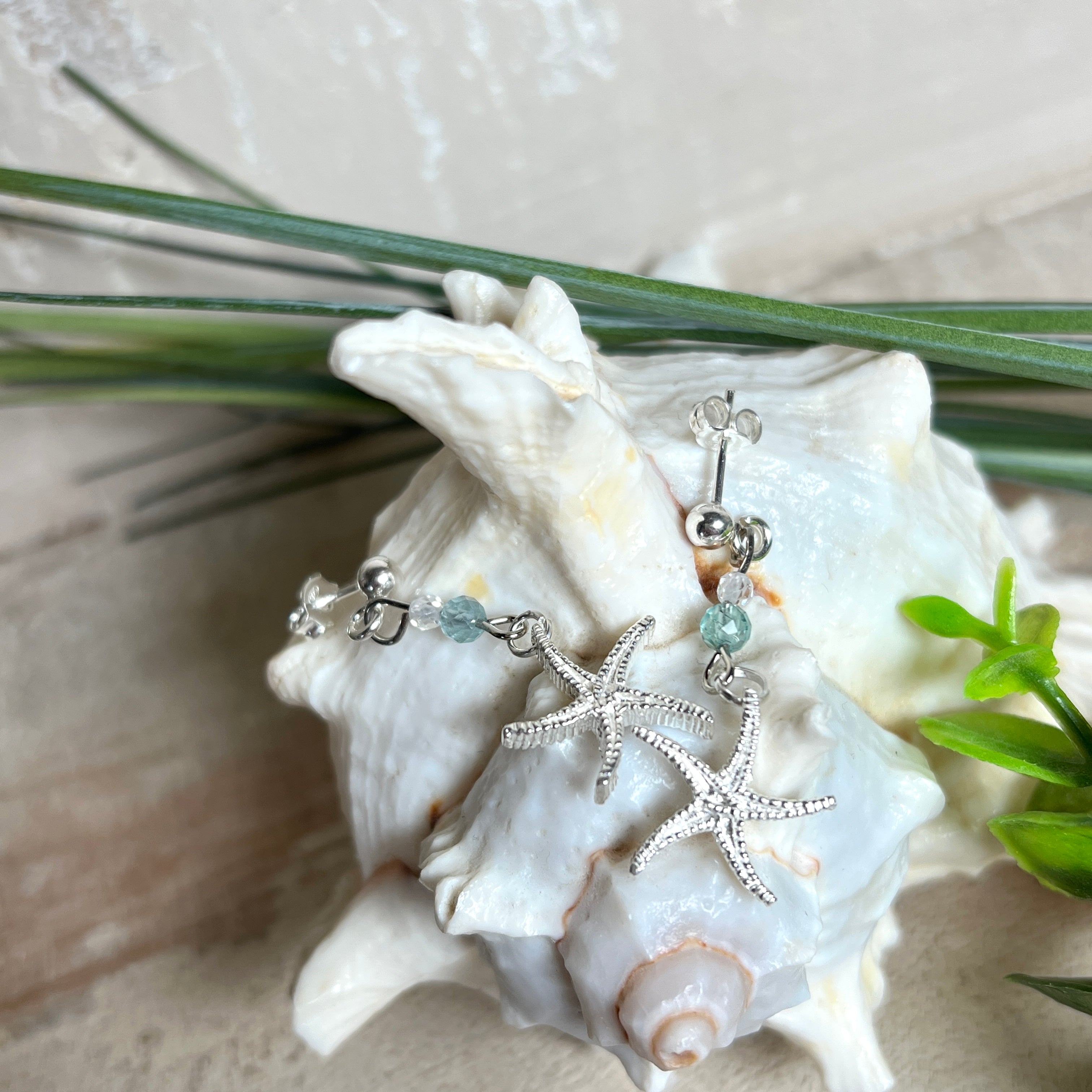 Edle „Ocean Star“ Ohrringe aus 925 Sterling Silber mit Seestern-Anhängern (18 × 17 mm), verziert mit einer aquablauen Apatitperle und funkelndem Zirkonia. Länge getragen: 45 mm. Maritime Schmuckstücke, die das Funkeln des Meeres einfangen – elegant, hochwertig und ein ideales Geschenk für Meeresliebhaber und Sommerträume.