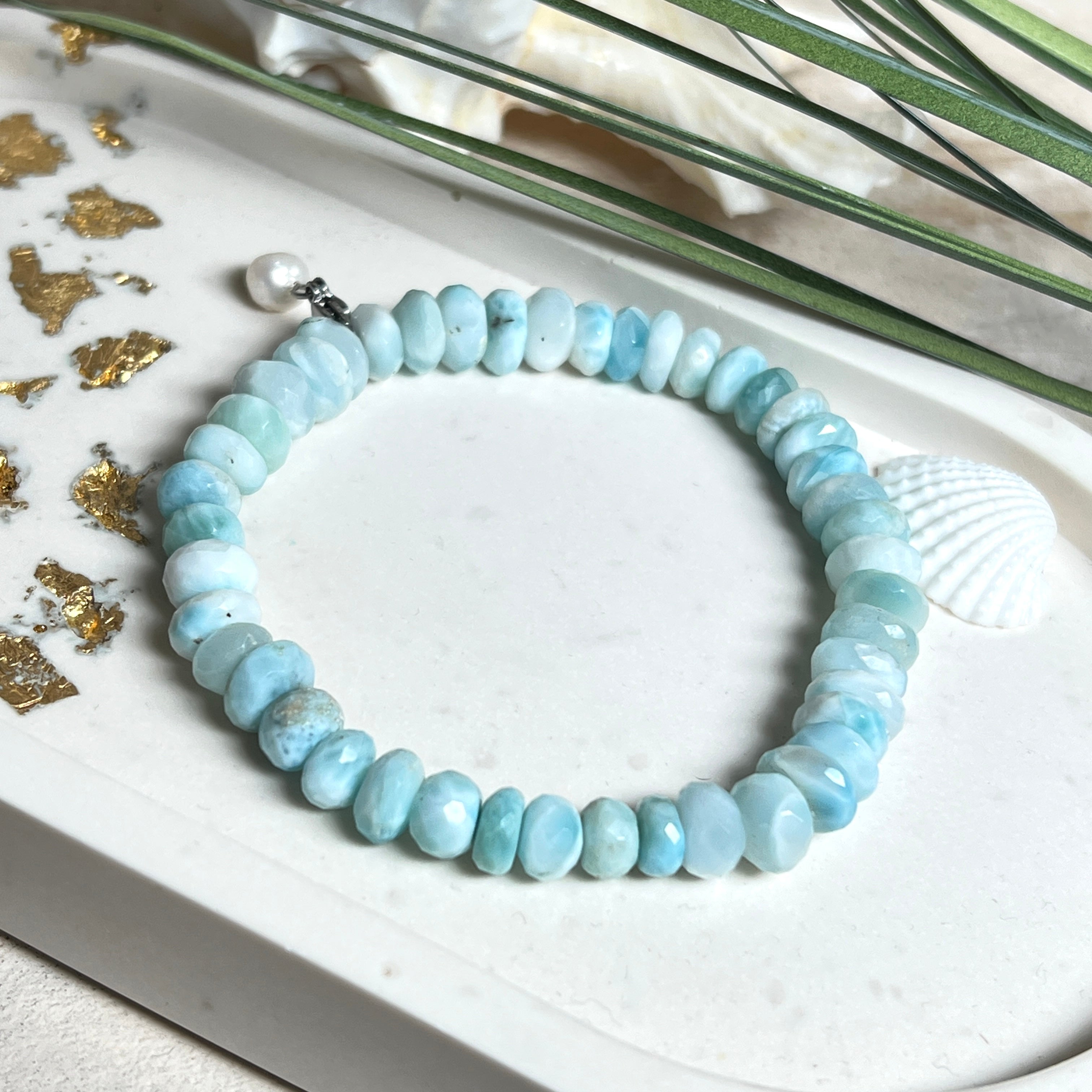 Handgefertigtes Armband aus seltenem Larimar mit facettierten, türkis-blauen Edelsteinperlen (Ø ca. 6–7 mm), elastischem Band und einem zarten Süßwasserperlen-Charm an Edelstahlkarabiner. Der wertvolle Larimar, auch „Stein des Atlantis“ genannt, gilt als Edelstein der Ruhe und Meeresverbundenheit.