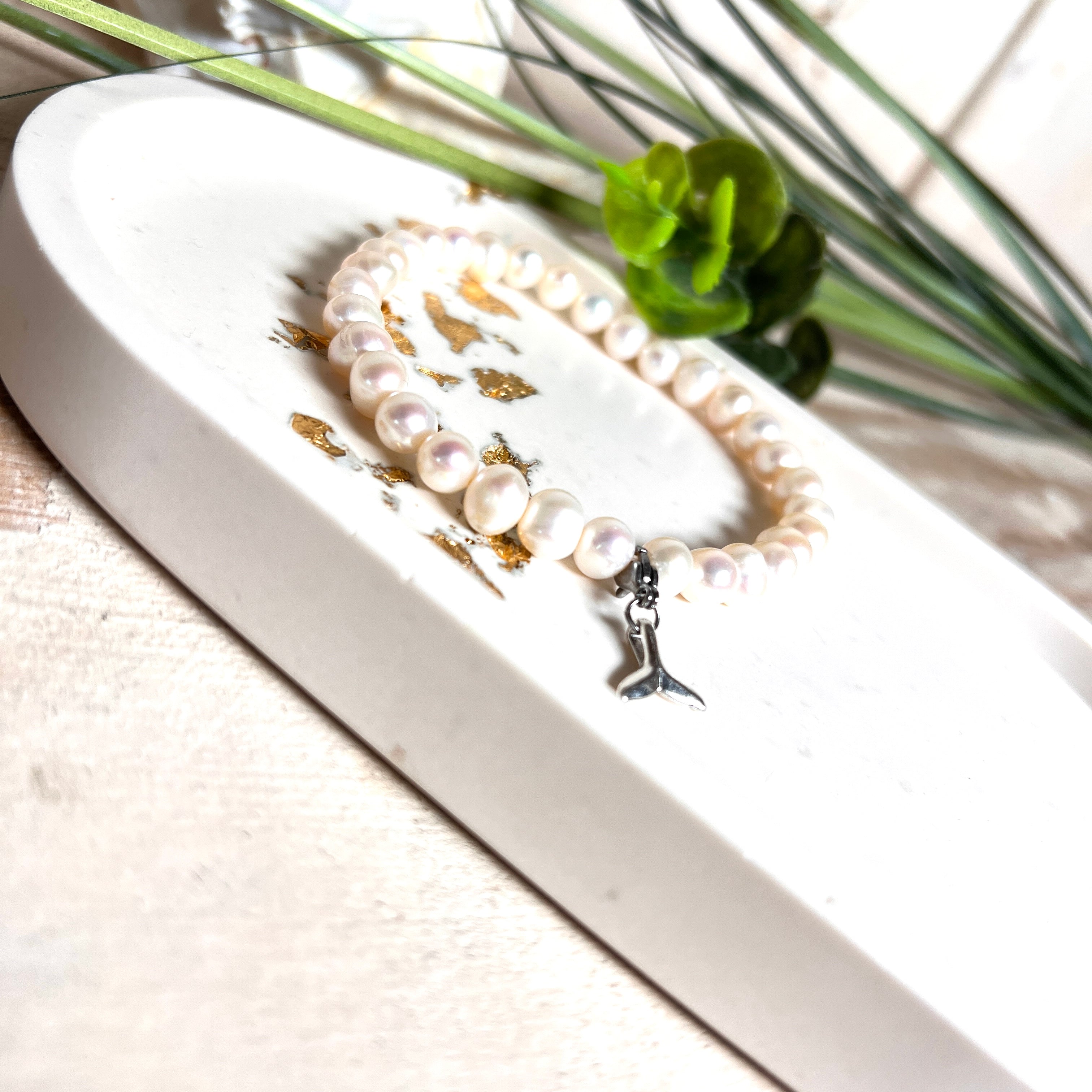 Handgefertigtes Armband aus echten Süßwasserperlen (ca. 6-7 mm), elastisch aufgezogen mit einem Edelstahl-Charm in Form einer Walflosse. Maritimes Design mit Bedeutung – stilvoll, natürlich und elegant. Größe ca. 17,5 cm. Ideal als Geschenk für Meeresliebhaberinnen oder für sich selbst.