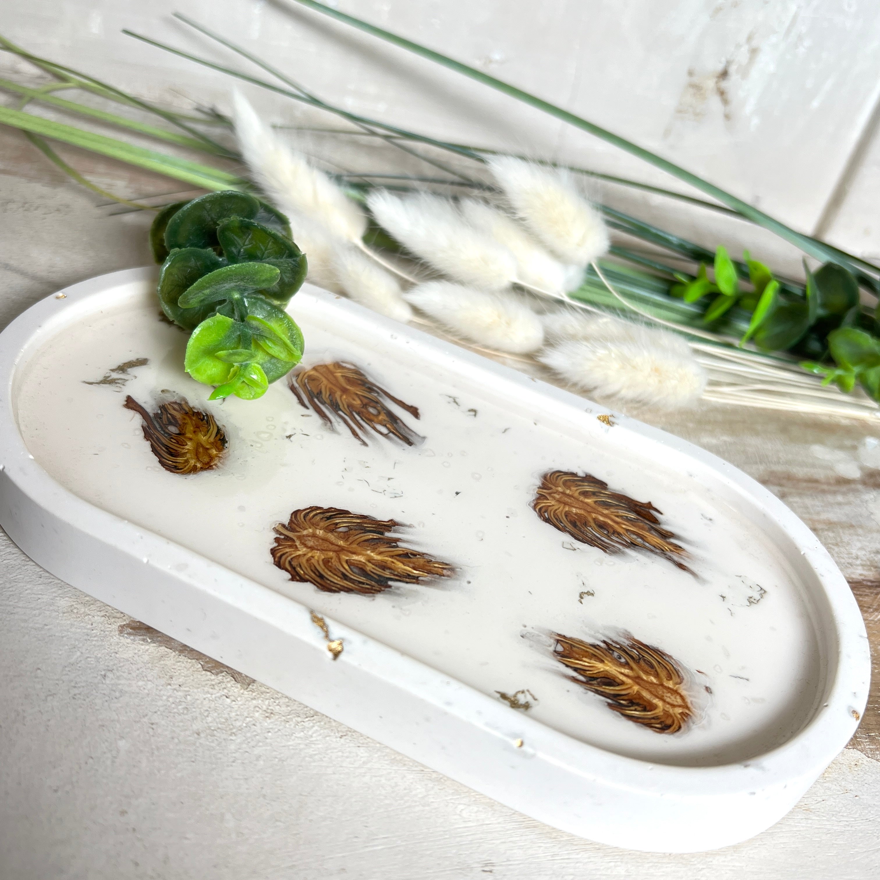Handgefertigtes Schmucktablett aus Jesmonite mit echten Zapfen, die in einer glänzenden Resin-Schicht eingebettet sind. Die ovale Form und die natürliche Farbgebung machen es zu einem stilvollen Wohnaccessoire. Mit rutschfesten Korkpunkten auf der Unterseite ideal als Ablage für Schmuck, Schlüssel oder Dekoartikel. Jeder Artikel ist ein Unikat aus Handarbeit – Lieferung ohne Dekoration.