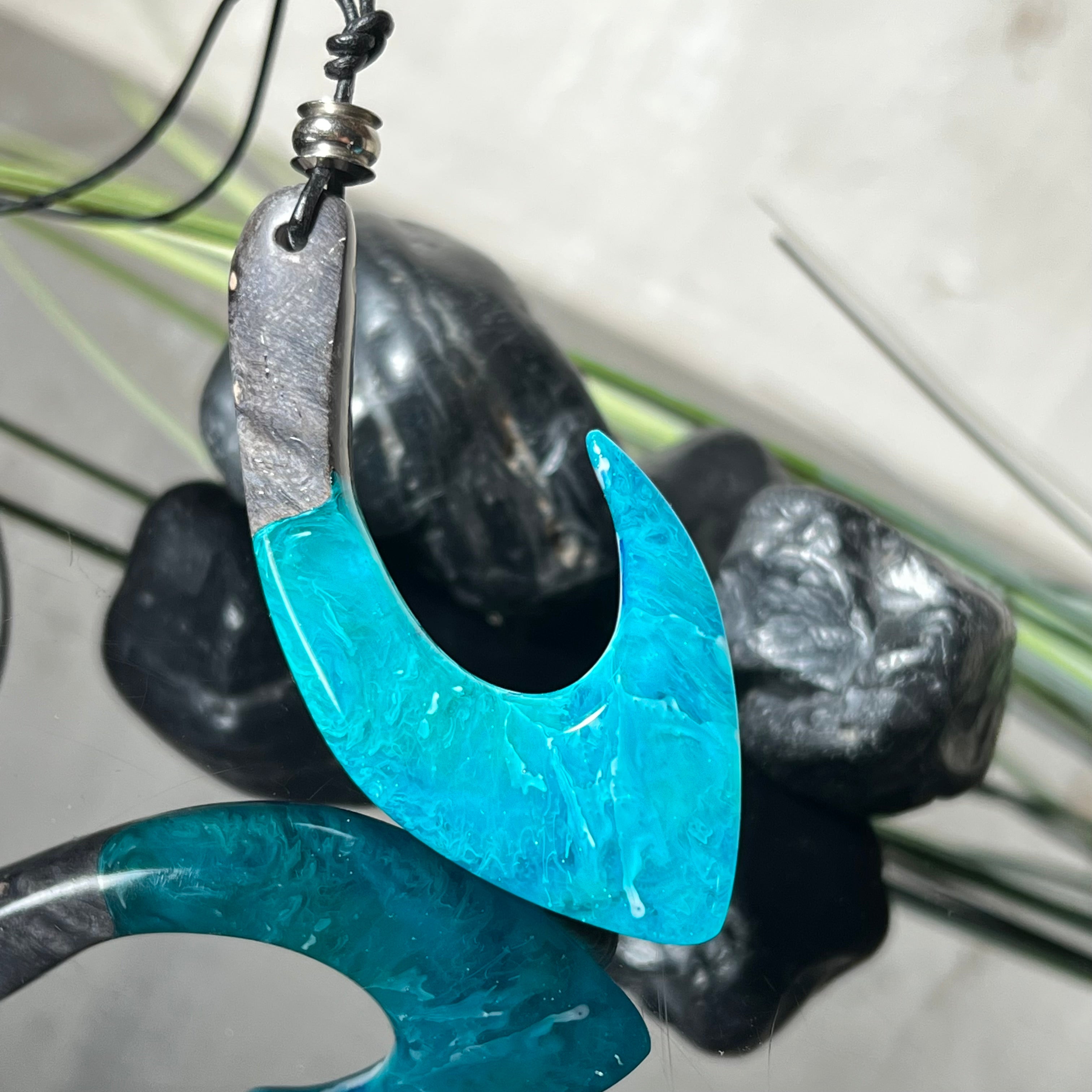 Handgefertigter Maori-Anhänger „Tangaroa Spirit“ in traditioneller Hakenform, gefertigt aus stabilisiertem Maserholz und ozeanblauem Harz. Die polierte Oberfläche bringt die natürlichen Maserungen und das tiefblaue Farbspiel besonders zur Geltung. Symbolisiert Schutz, Stärke und die Verbundenheit zum Meer. Verstellbares Lederband mit Schiebeknoten und dekorativen Holz- sowie Metallperlen – ideal als kraftvoller Talisman oder Geschenk.