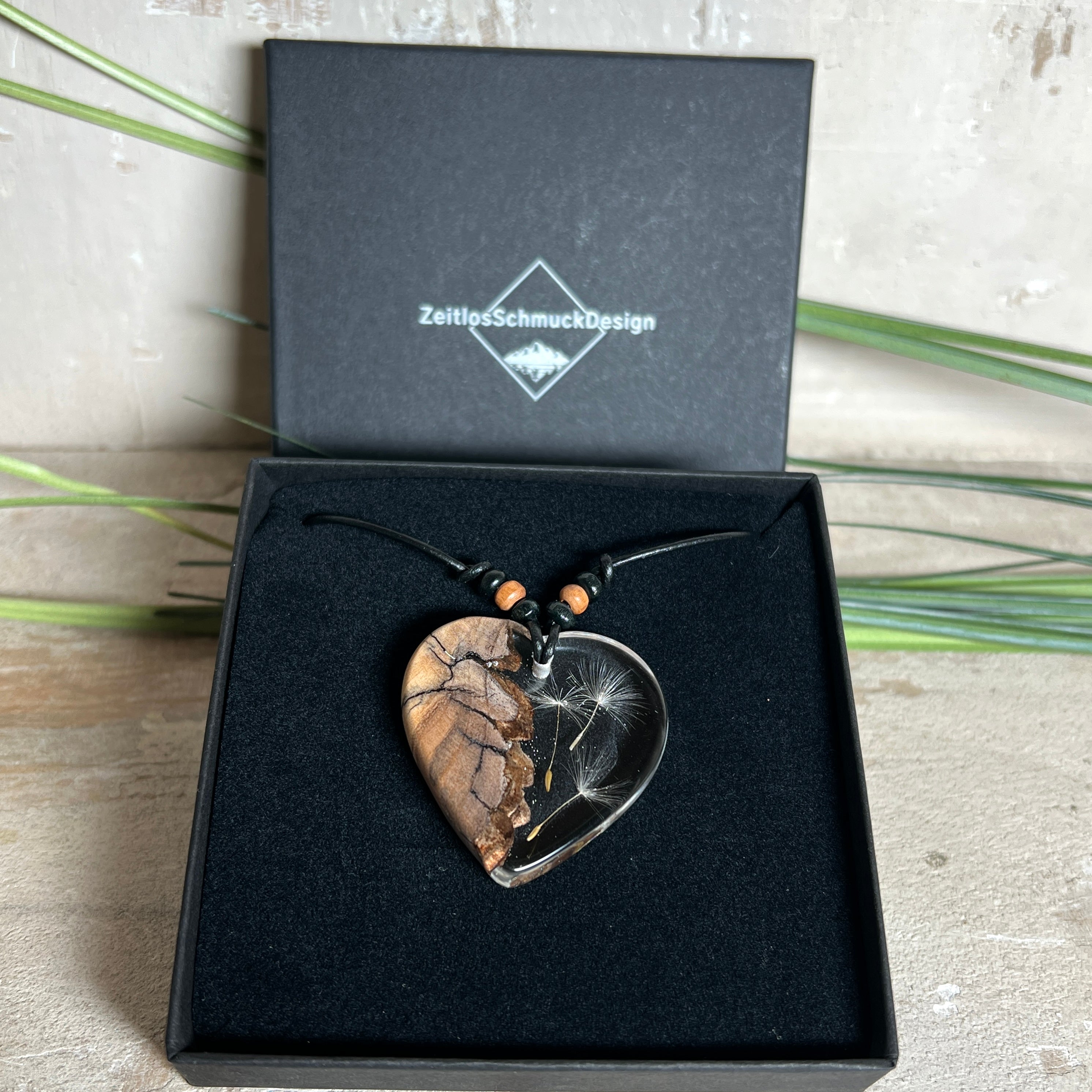 „Handgefertigter Herzanhänger aus Olivenholz und klarem Harz mit echter Pusteblume. Der Anhänger (ca. 3,5 × 3,5 cm) hängt an einem verstellbaren Lederband (23–43 cm) mit Holzperlen. Symbol für Wünsche und Glück, sorgfältig in Handarbeit gegossen, gesägt, geschliffen und poliert. Ein einzigartiger, naturinspirierter Anhänger – ideal als Geschenk oder persönlicher Talisman.“