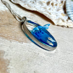 „Riffschatz“ – ovaler Harz-Anhänger mit plastischer 3D-Welle in Blau/Türkis, weißer Schaumkrone und Muschel-/Korallen-Stickern am Grund. Die Sticker sind unter klarem Harz versiegelt. Silber-Legierung, ca. 3,9 × 2,3 cm, an einer ca. 56 cm langen versilberten Kette. Handgefertigt, hochglänzend, jedes Stück ein Unikat.