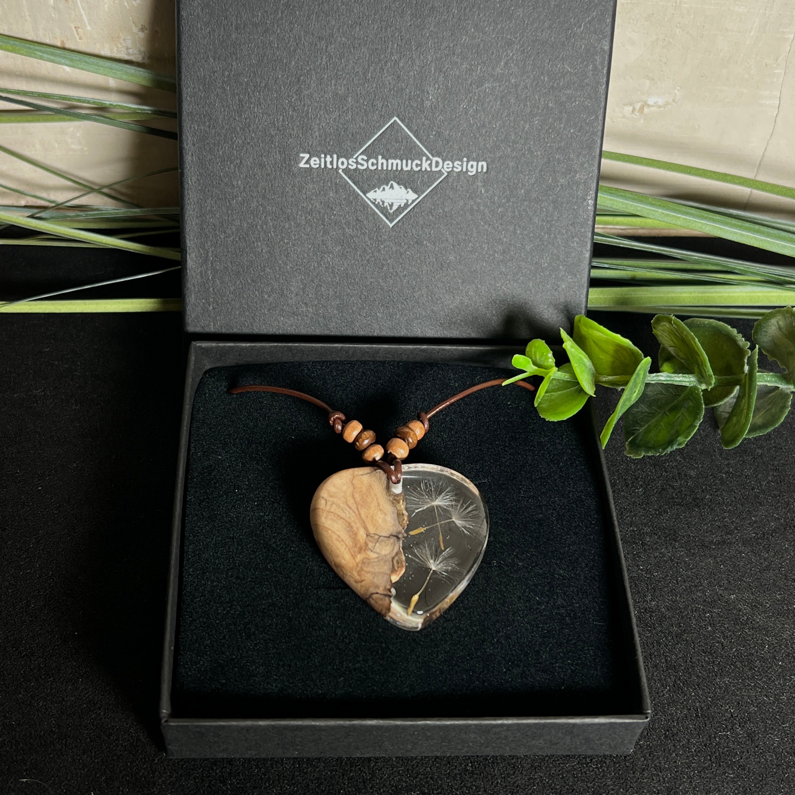 Handgefertigter Herzanhänger aus Olivenholz und klarem Harz mit echten Pusteblumen. Der Anhänger misst ca. 3,5 cm, das Lederband ist verstellbar von 23–43 cm und mit kleinen Holzperlen verziert. Ein natürliches Unikat, Symbol für Wünsche und Glück – sorgfältig gegossen, gesägt, geschliffen und poliert.