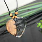 Handgefertigter Herzanhänger aus warm gemasertem Olivenholz und kristallklarem Epoxidharz mit schwebenden Pusteblumensamen. Schwarzes, verstellbares Lederband mit Schiebeknoten und naturfarbenen Holzperlen, Anhänger ca. 3,5 × 3,3 cm. Naturnaher Unikatschmuck von ZeitlosSchmuckDesign.