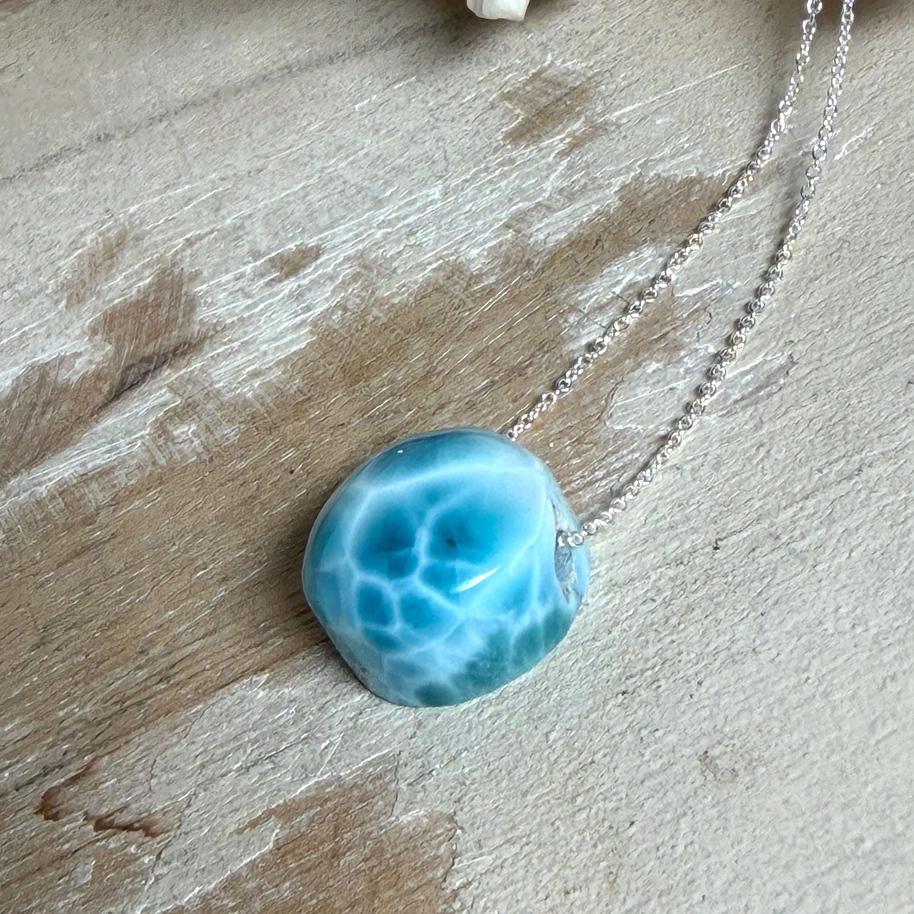 Feine Kette mit rundem Larimar-Cabochon in AA-Qualität. Der ca. 20 mm große Stein zeigt ein intensives Blau mit hellen, netzartigen Zeichnungen und ist mittig mit einer 2,5 mm Bohrung versehen, durch die eine zarte 925 Silberkette (45 cm, ca. 1 mm stark) geführt wird. 