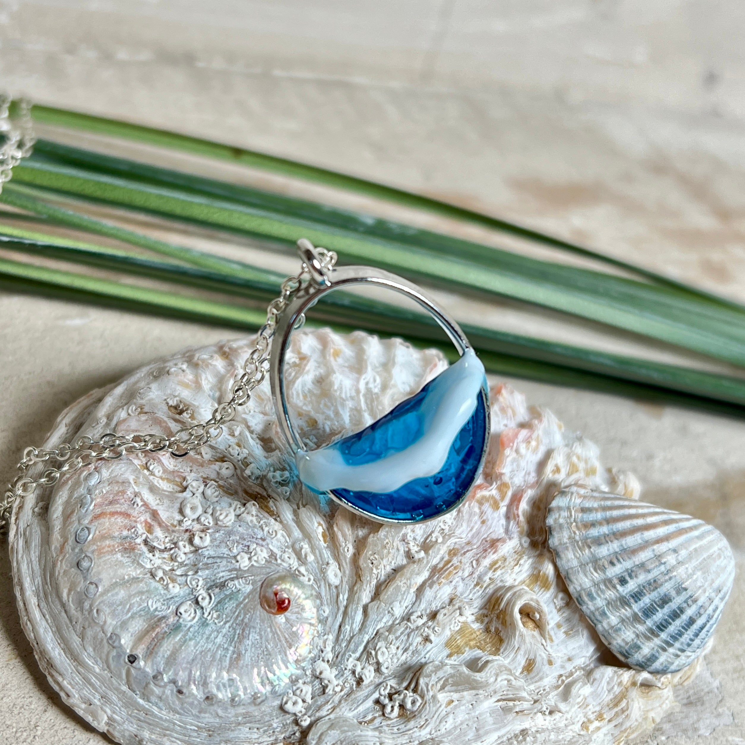 Ovale Halskette „Ocean Crest“ mit 3D-Welle: handgefertigter Harz-Anhänger in Silber-Legierung, Farbverlauf von Tiefblau zu Türkis mit weißer Schaumkrone. Größe ca. 3,9 × 2,3 cm, an einer ca. 56 cm langen versilberten Kette. Glänzende Oberfläche, maritimer Look, Unikat-Handarbeit.