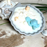 andgefertigte Kerze „Ozeanfreund“ in Jesmonite-Schale (ca. 11 cm). Gefüllt mit nachhaltigem Sojawachs, dekoriert mit echten Muscheln, handgegossenen Wachsmuscheln und einer türkisfarbenen Wachsschildkröte. Maritime Kerze – einzigartig, dekorativ und perfekt als Geschenk oder als Meeres-Deko.