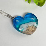 Ein herzförmiger Anhänger mit einer ganzen Ozeanwelt darin: Welle, Sand und Seestern in leuchtendem Blau und Türkis – handgegossen, einzigartig, unvergesslich. Mit versilberter Kette (46 cm) und Edelstahl-Karabiner.