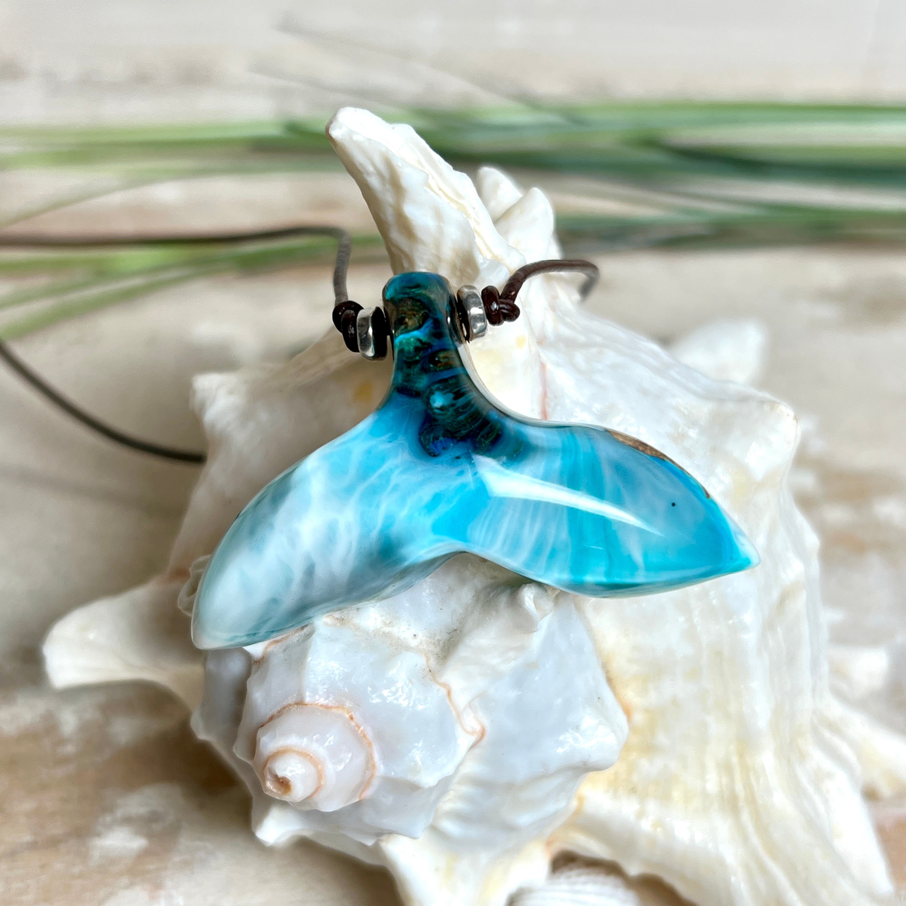 Walflossen-Anhänger „Flossenklang“ – handgefertigtes Unikat aus Maserholz und türkis-blau-grauen und weißem Harz. Die elegant geschwungene Form erinnert an die Flosse eines Wals und symbolisiert Freiheit, Stärke und Naturverbundenheit. Mit verstellbarem braunem Lederband gefertigt, ist jedes Stück ein individuelles Schmuckstück für Meeresliebhaber und Natursuchende. Maritimer Halsschmuck, inspiriert vom Ozean, glatt poliert und mit Liebe zum Detail von Hand gearbeitet.