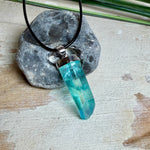 Nahaufnahme einer handgefertigten Halskette mit Aqua Aura Rohkristall: naturbelassener, sechskantiger Bergkristall mit goldbedampfter Aqua-Beschichtung in Türkisblau, gefasst in 925er Silber und getragen an einer schwarzen Lederkette mit Edelstahl-Karabiner und Verlängerungskettchen.