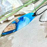 Handgefertigter Surfbrett-Anhänger „Ocean Glide“ aus Maserholz und Epoxidharz in verschiedenen Blau-, und Weißtönen. Der ca. 6,5 × 2 cm große Anhänger wird an einem verstellbaren Lederband (26–46 cm) mit Holzperlen geliefert. Ein maritimes Unikat mit natürlicher Holzmaserung, das die Schönheit des Meeres einfängt.